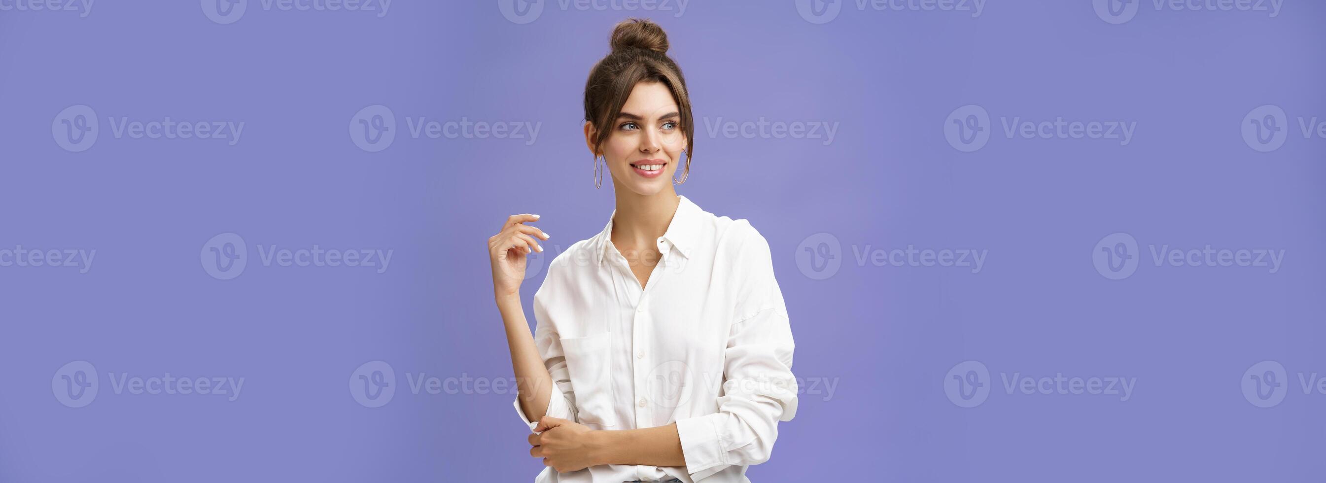 Feminine and stylish modern charming girl with gapped teeth and pimple posing in trendy white blouse and round earrings gazing left charmed and sensual with cute smile over purple background photo