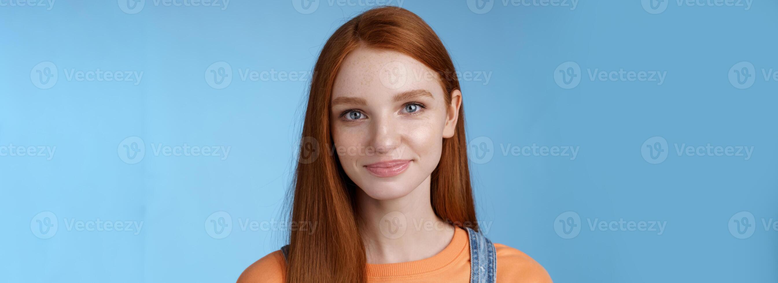 Outgoing young redhead girl blue eyes wearing orange t-shirt overalls smiling pleasantly casually talking standing good mood joyful emotions blue background, listening interesting conversation photo