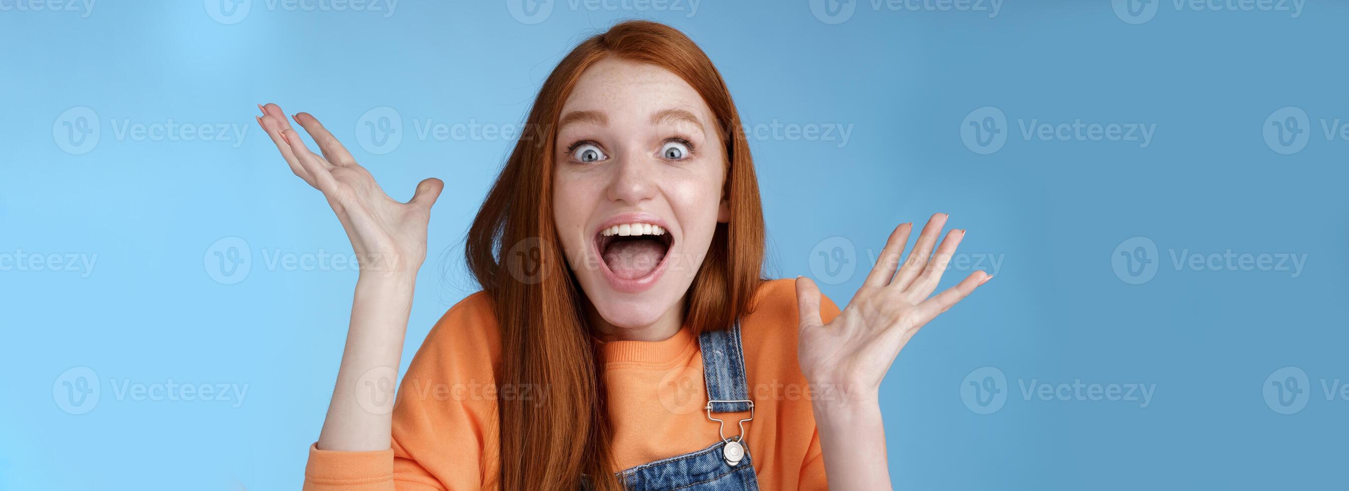 Surprised astonished sensitive overwhelmed young happy redhead girl receive incredible fantastic prize wide eyes astonished raising hands triumphing win lottery celebrating joyfully photo