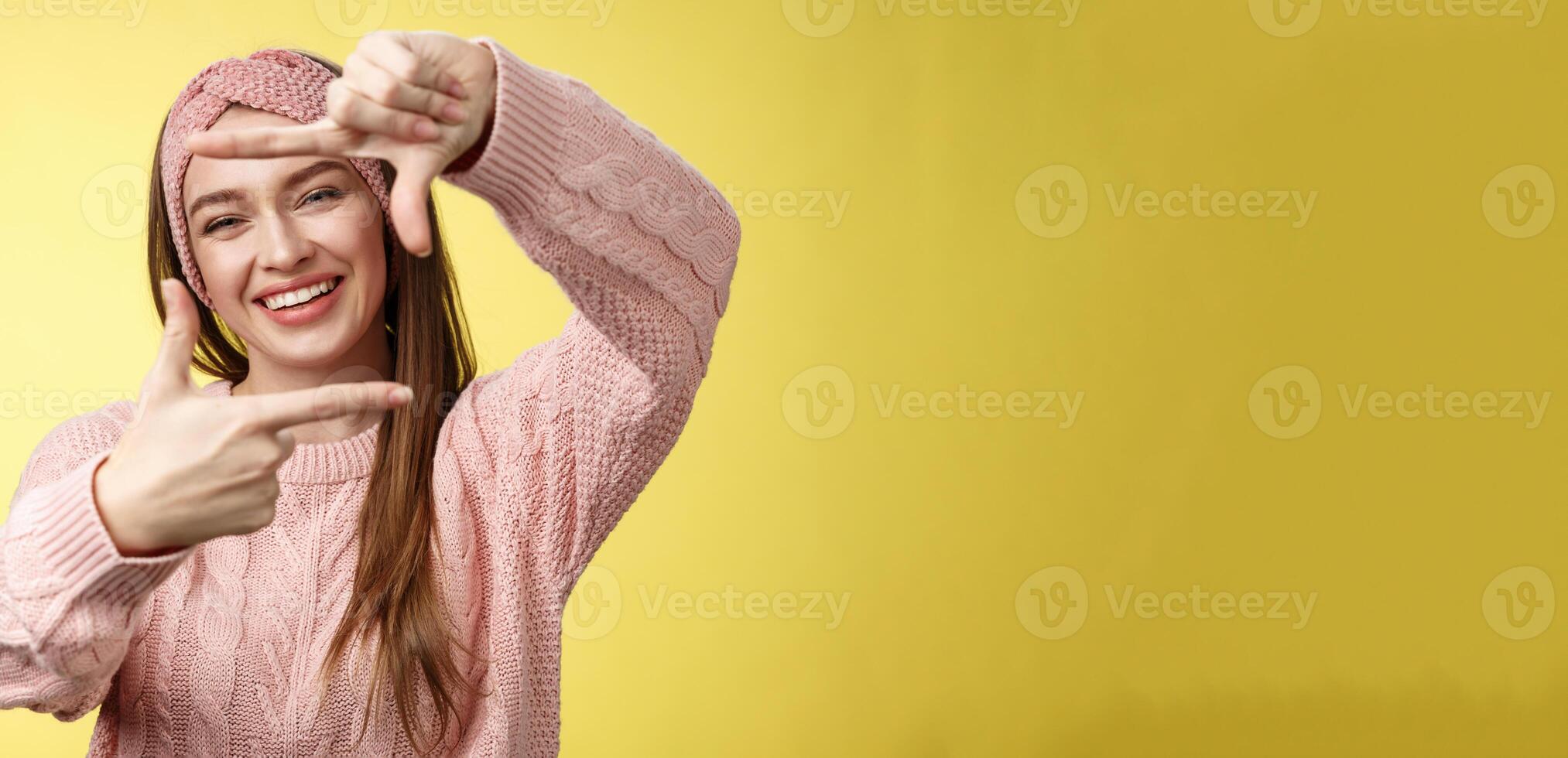 Charming outgoing, happy girl smiling cheerful, making frame of fingers looking through it excited and joyful, grinning, planning future, picturing how put furniture, posing cute over yellow wall photo