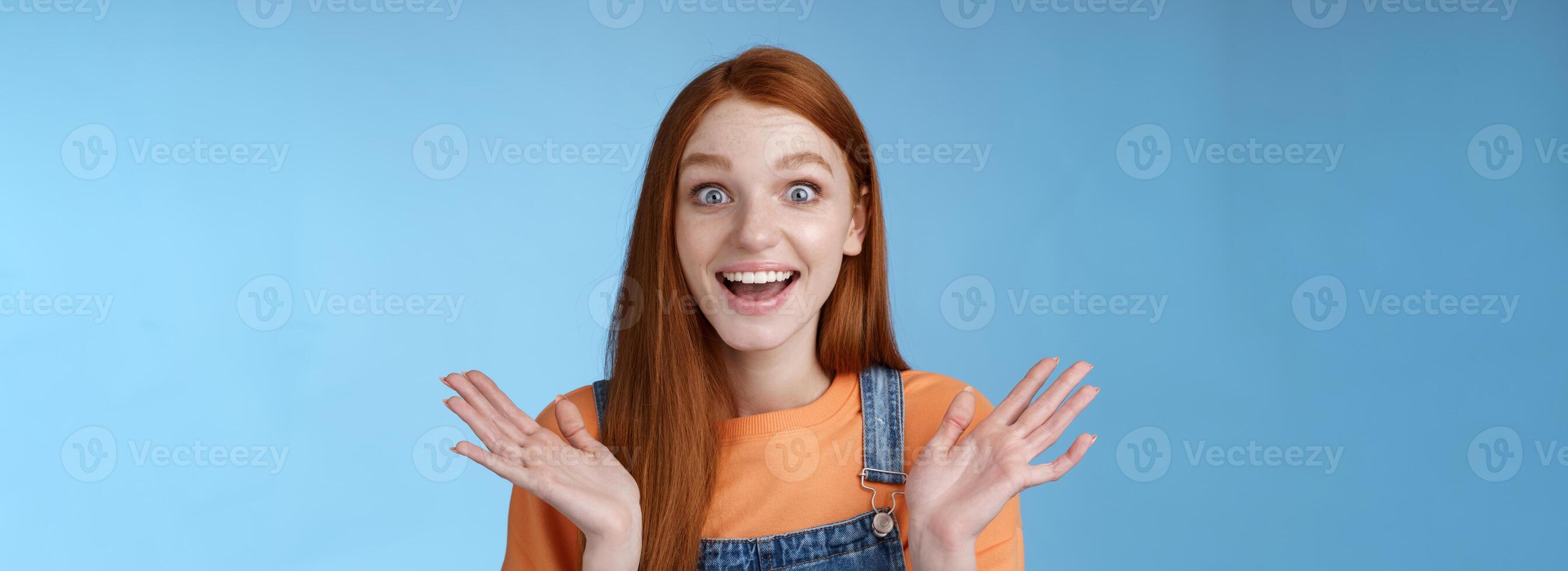 Surprised delighted happy friendly-looking amused redhead female friend learn incredible good news congratulating girlfriend fascinated wide eyes camera joyfully clap hands amazed, blue background photo