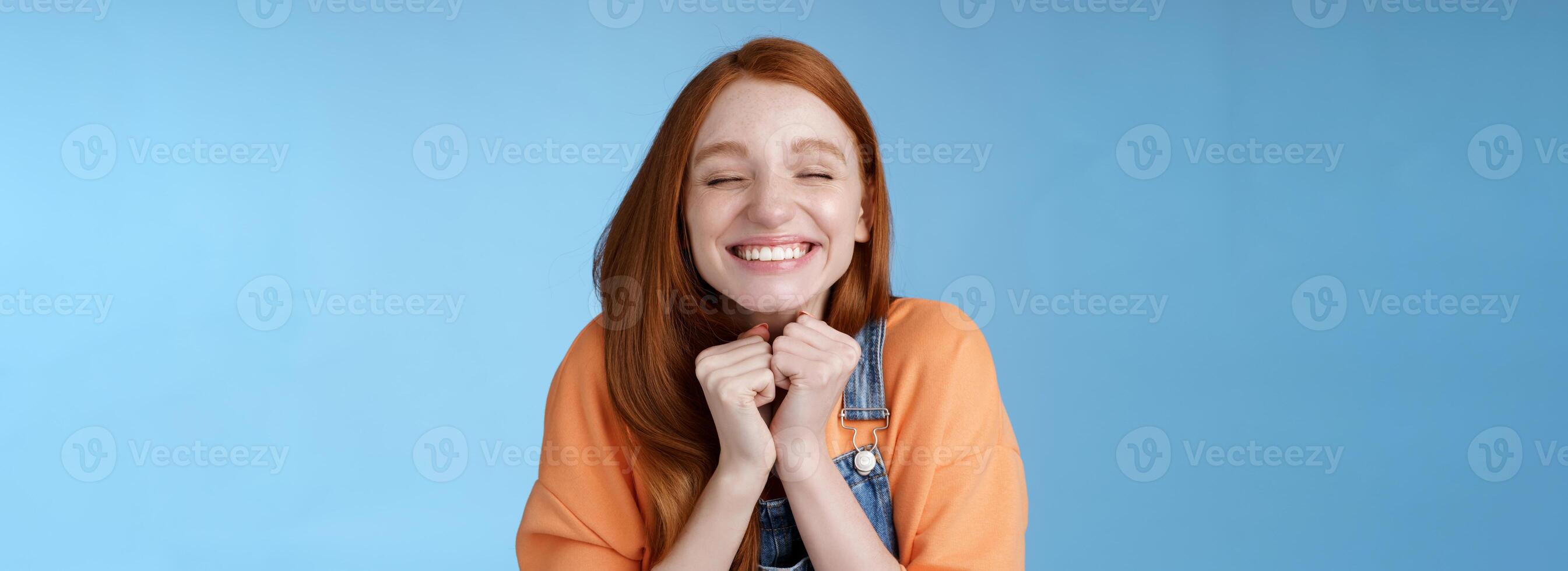 Eager rejoicing thrilled pretty young redhead girl close eyes dreamy smiling receive great result scholarchip triumphing joyfully grinning squeez hands excited, standing blue background very happy photo