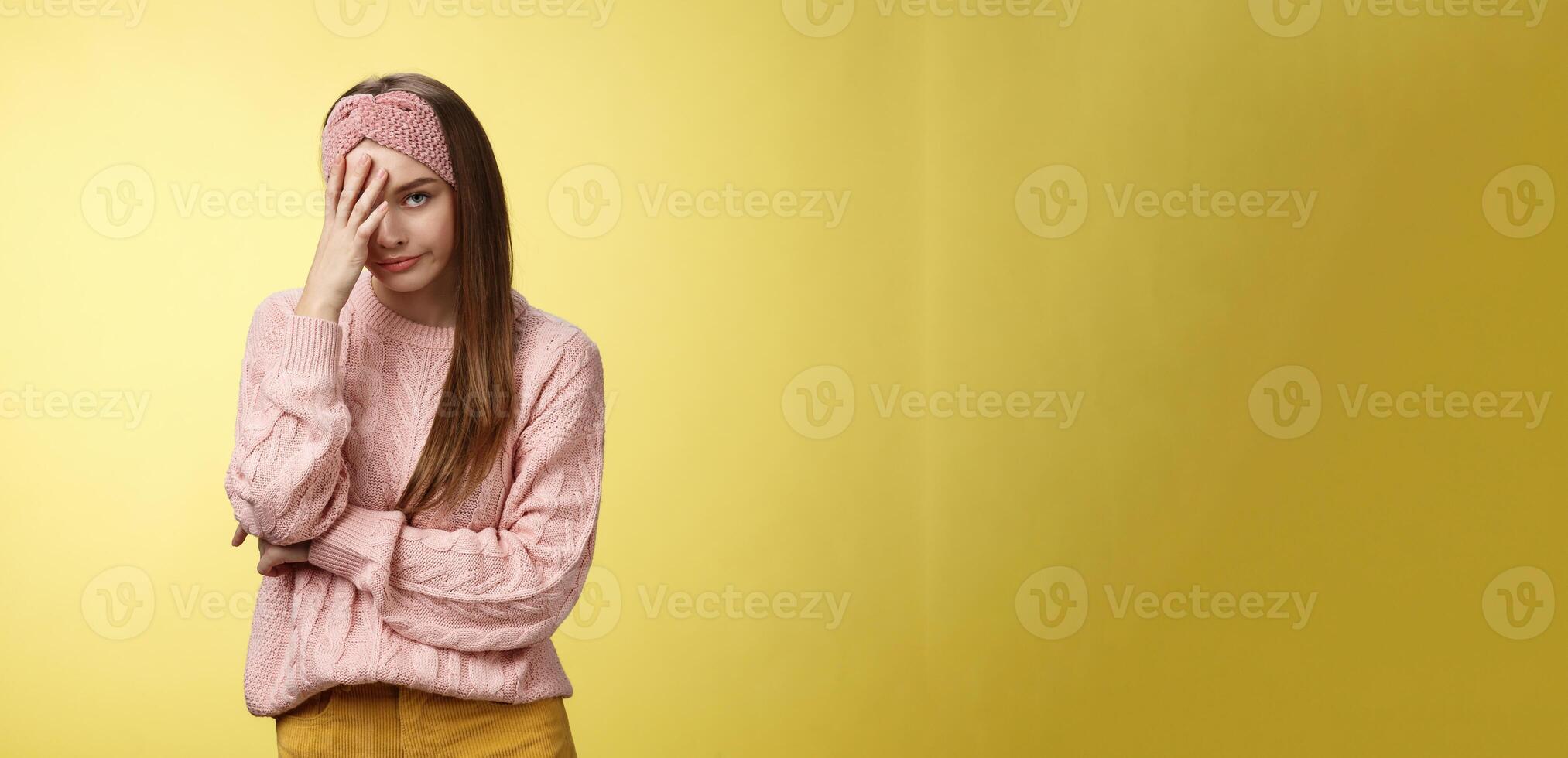 Woman facepalming covering face annoyed, bothered and inrritated, smirking looking with dismay, pissed off, posing unhappy displeased, staring indignant and upset posing tired over yellow background photo