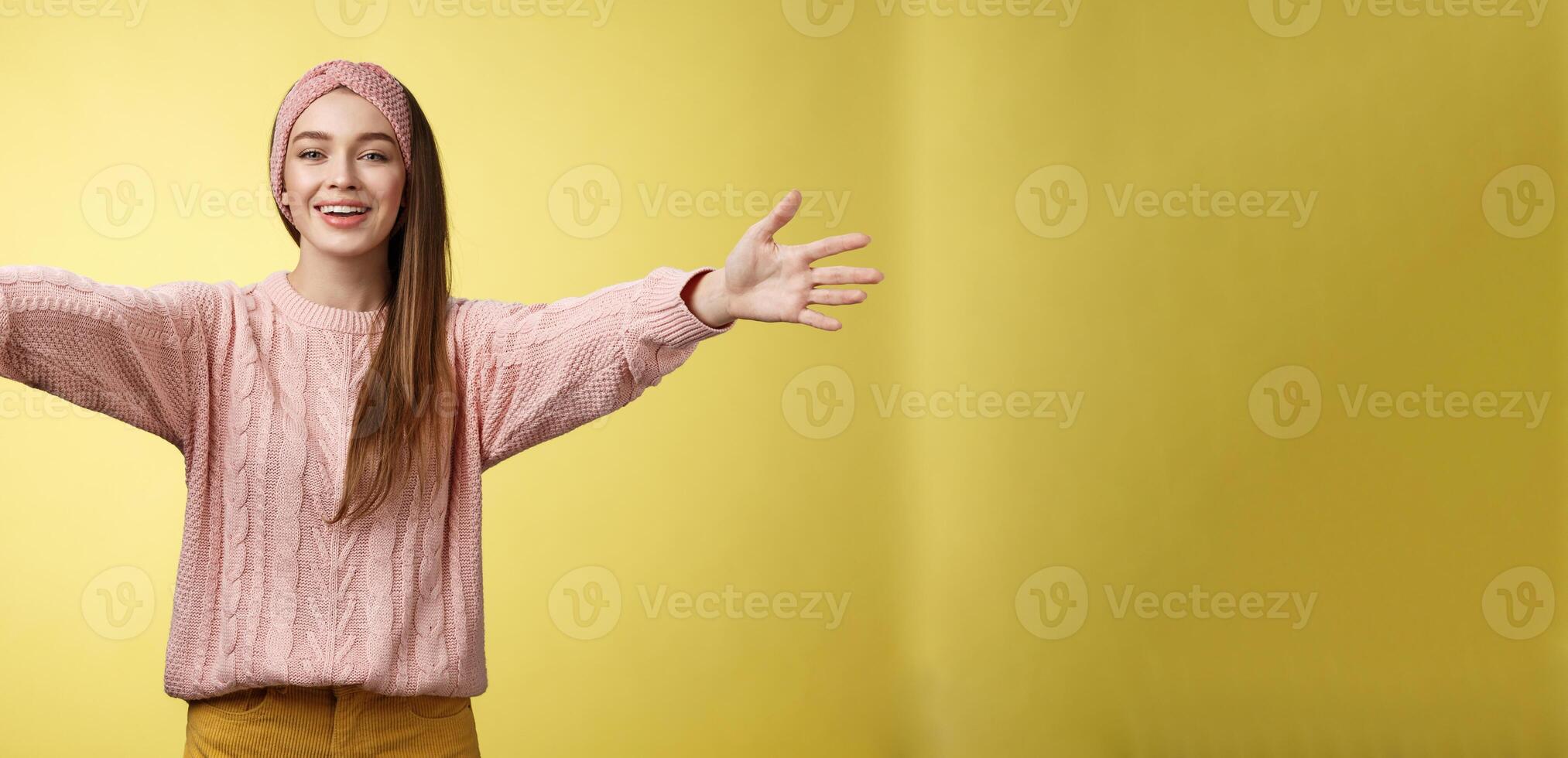 atractivo simpático positivo joven europeo mujer vistiendo suéter, venda acogedor extendiendo brazos y sonriente a cámara dando abrazos, abraza amigos, acurrucarse en contra amarillo antecedentes foto