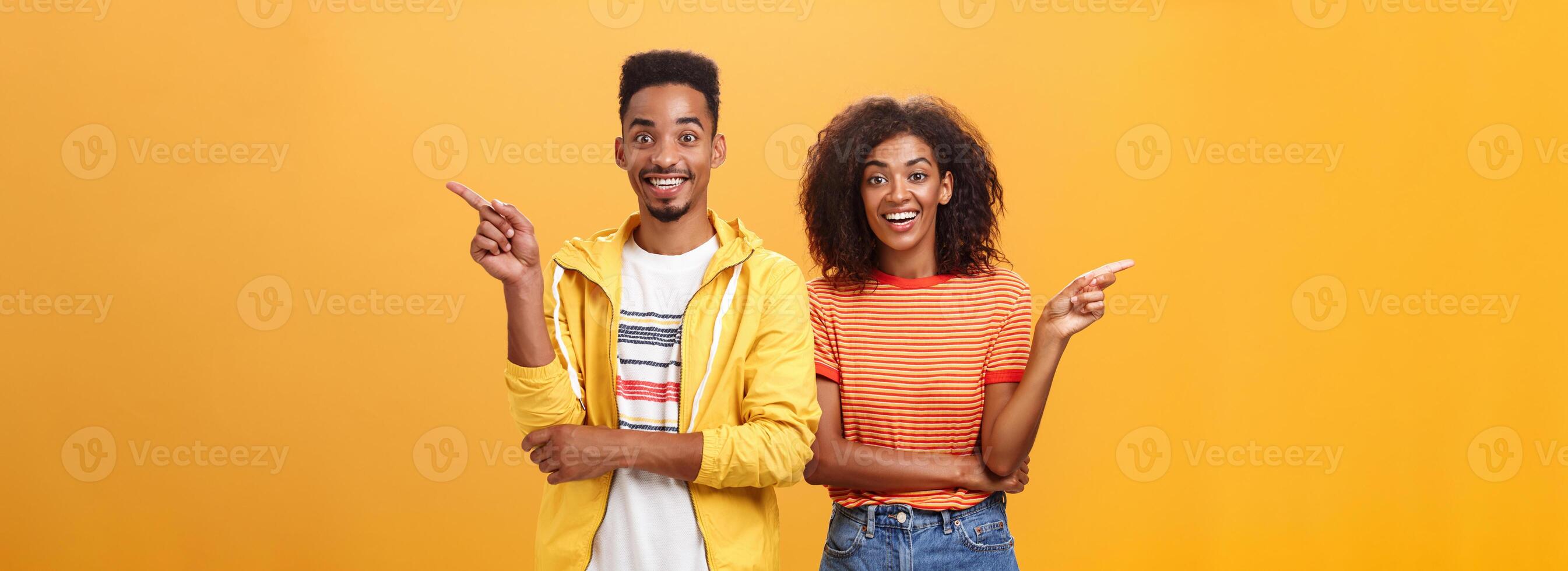 Which one telling true. Joyful and friendly good-looking couple, african american woman pointing left and dark-skinned guy right smiling broadly at camera giving advices but disagree with each other photo