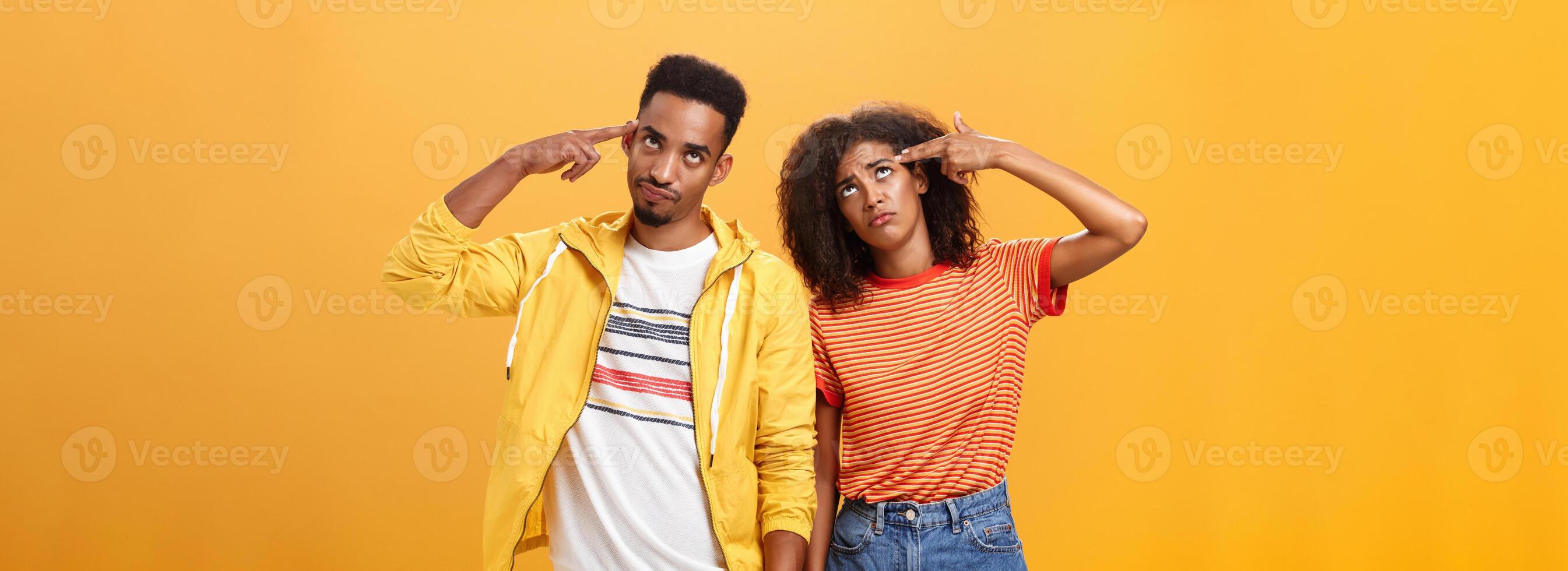 Pair of african american lovers getting annoyed with parents scolding, teaching them how live sexual life rolling eyes up from irritation holding finger gun near temples standing close to each other photo