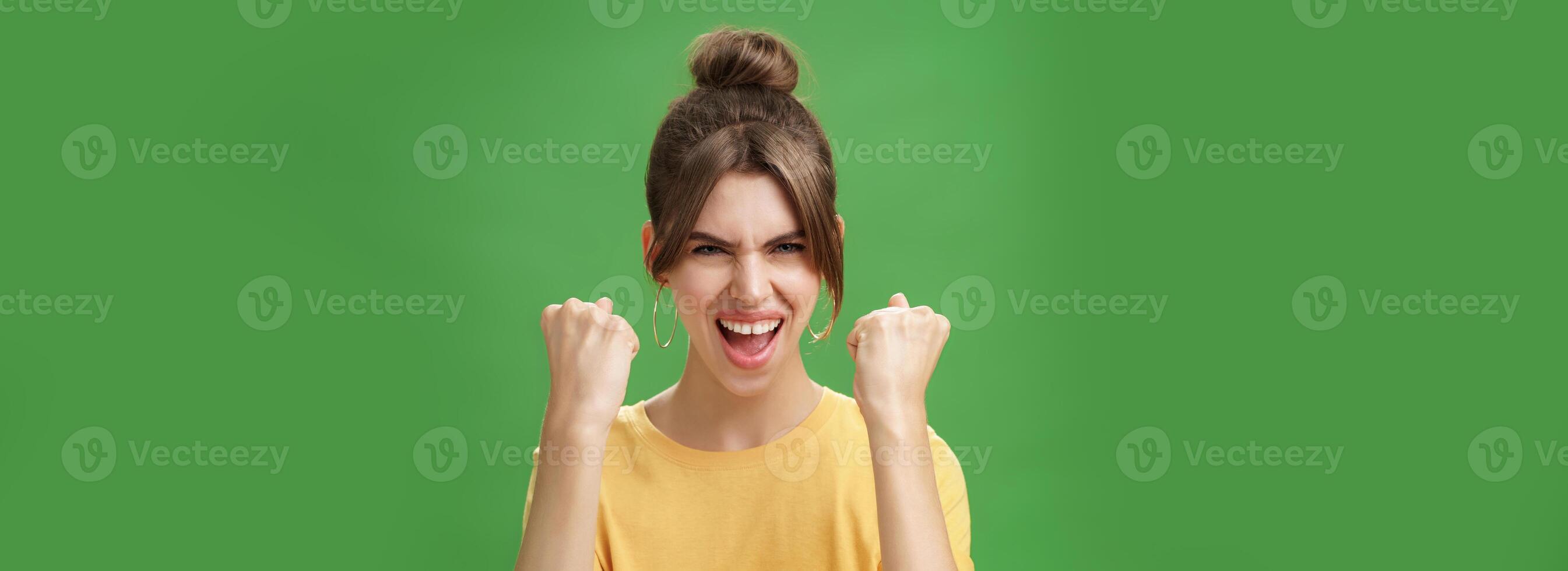 mujer con espíritu de ganador levantamiento apretado puños sonriente emocionado y apoyo aplausos siendo Listo para gimnasio ejercitado abucheos confidentes con grito mirando atrevido a cámara terminado verde pared foto