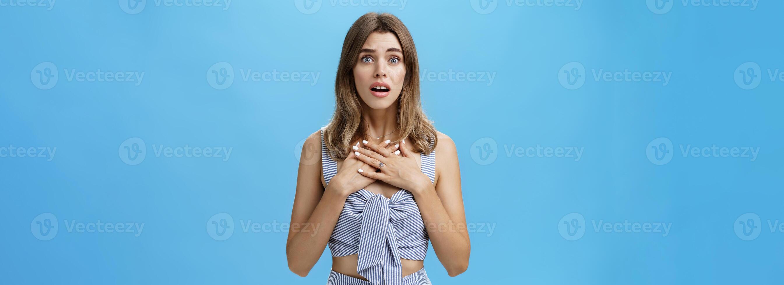 Waist-up shot of woman feeling bad for friend empathizing hearing shocking story gasping opening mouth and looking speechless holding palms on breast standing intense and nervous over blue wall photo