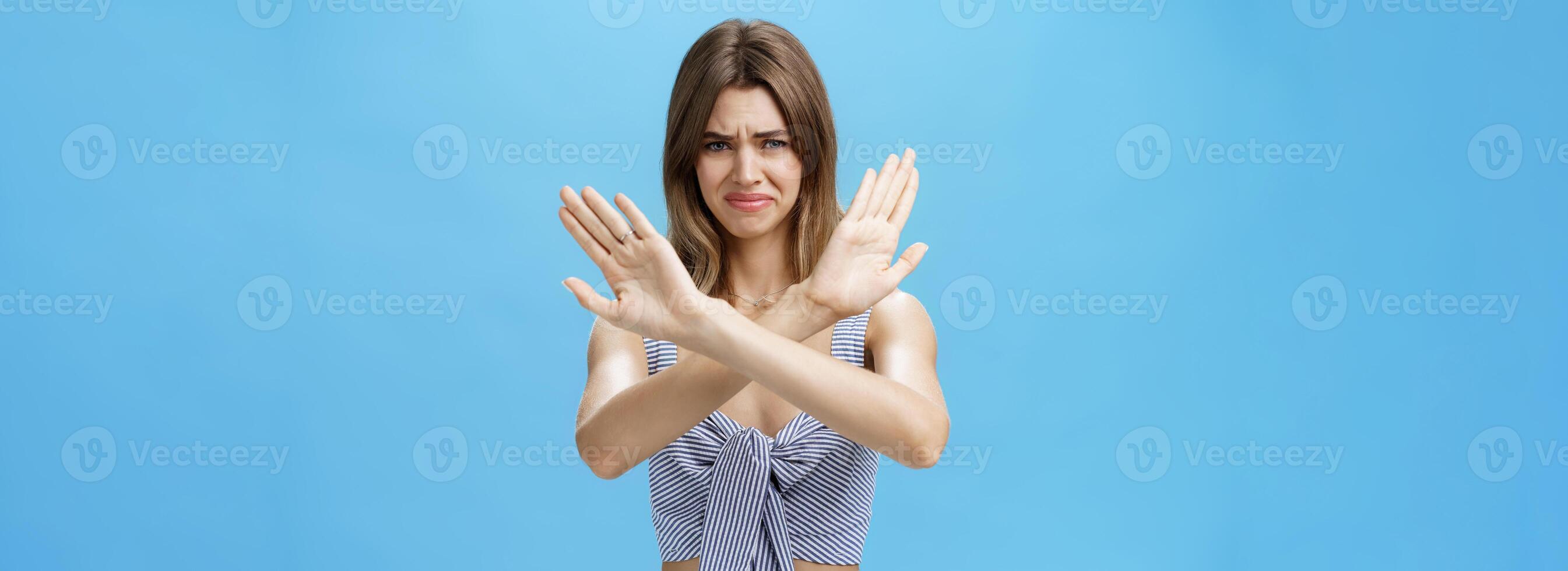 Woman refusing it disgusting dish. Displeased young cute woman in matching clothes crossing hands over body in stop gesture frowning and grimacing from aversion and dislike looking at creepy object photo