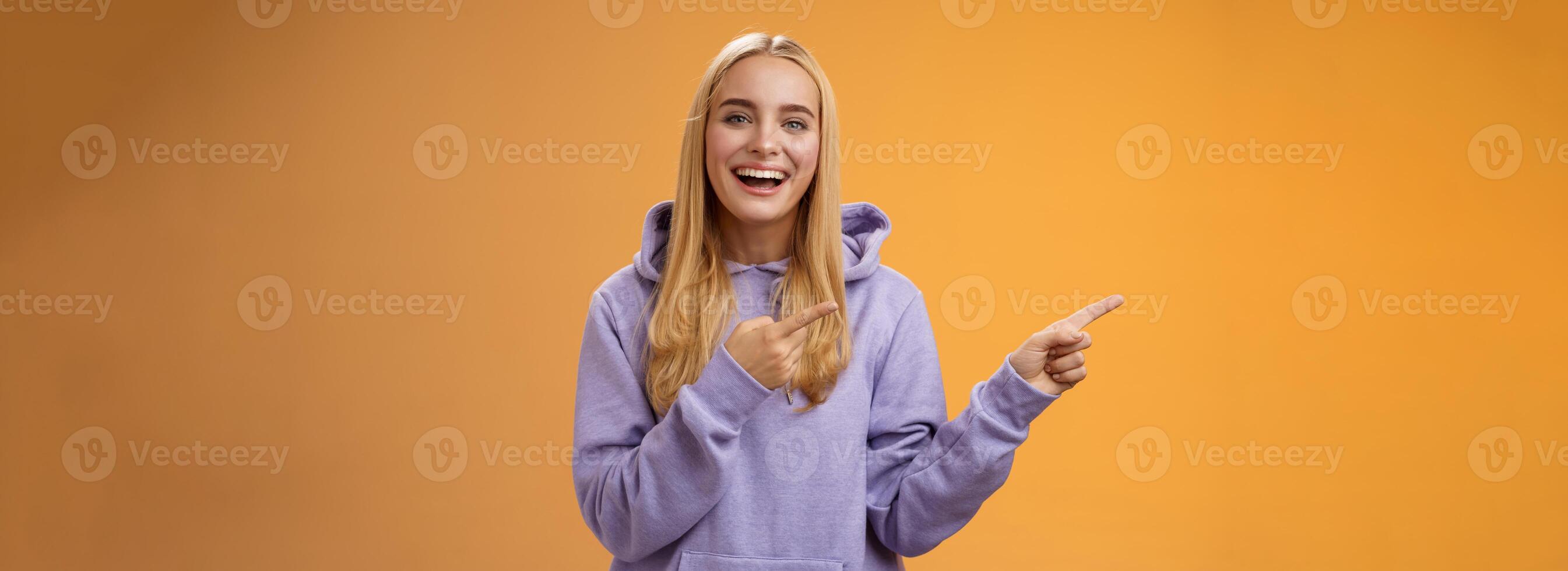 Charismatic firendly good-looking blond young female student pointing left discussing awesome new restaurant suggesting friend go check out laughing smiling happily, orange background photo