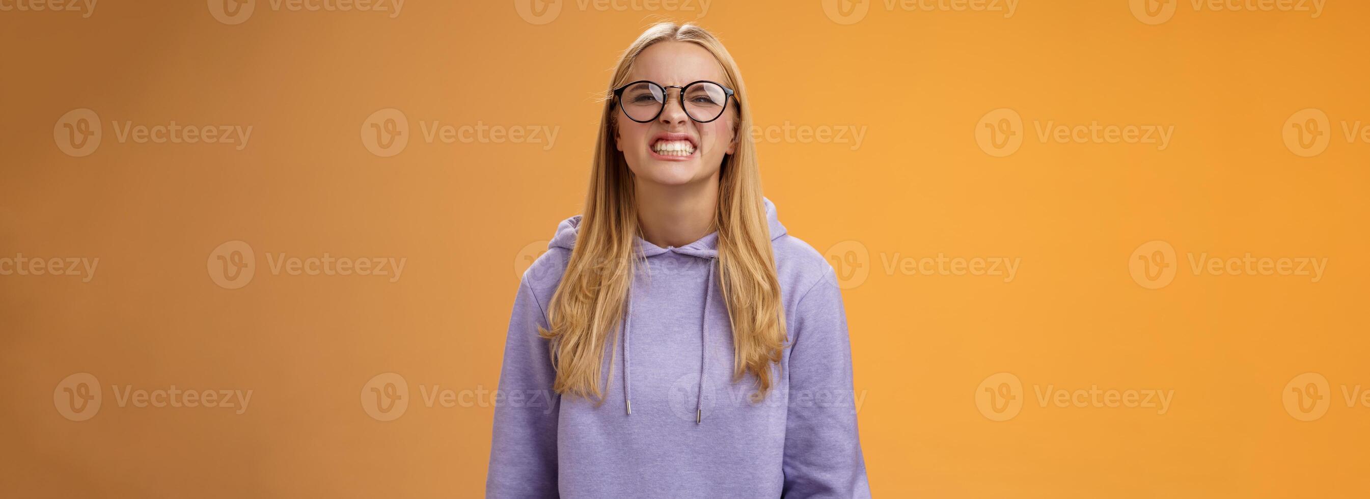 Blond girl show teeth warn can stand herself bite, fool around grimacing funny wearing purple hoodie glasses standing orange background better not mess with me, pranking friend have fun photo