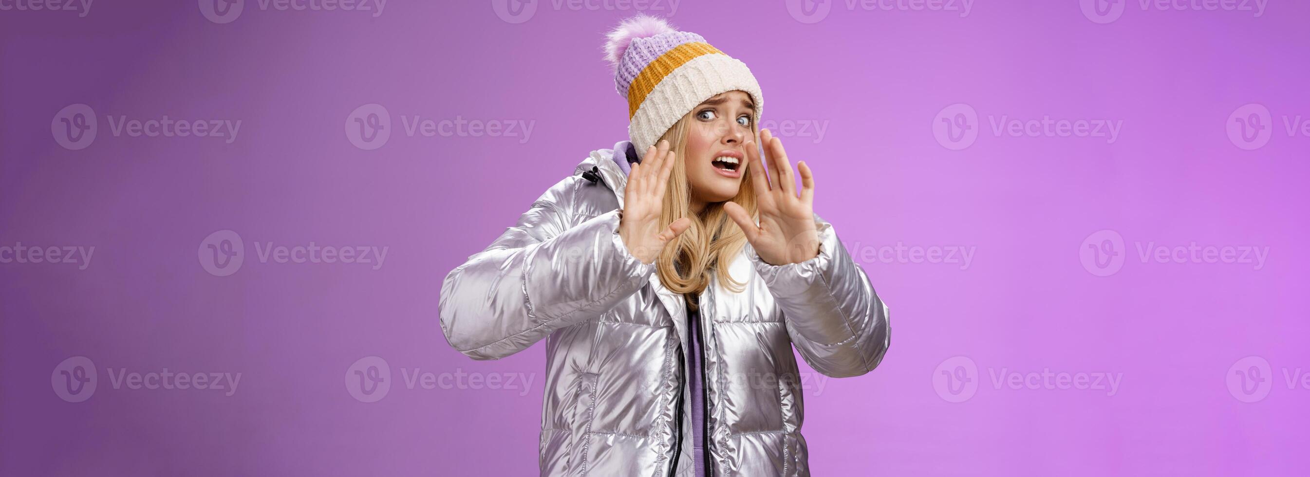 Afraid intense uncomfortable young fair-haired woman in winter hat silver stylish dress run away raise hands self-defense turn head away scared friend spill drink new outfit, purple background photo