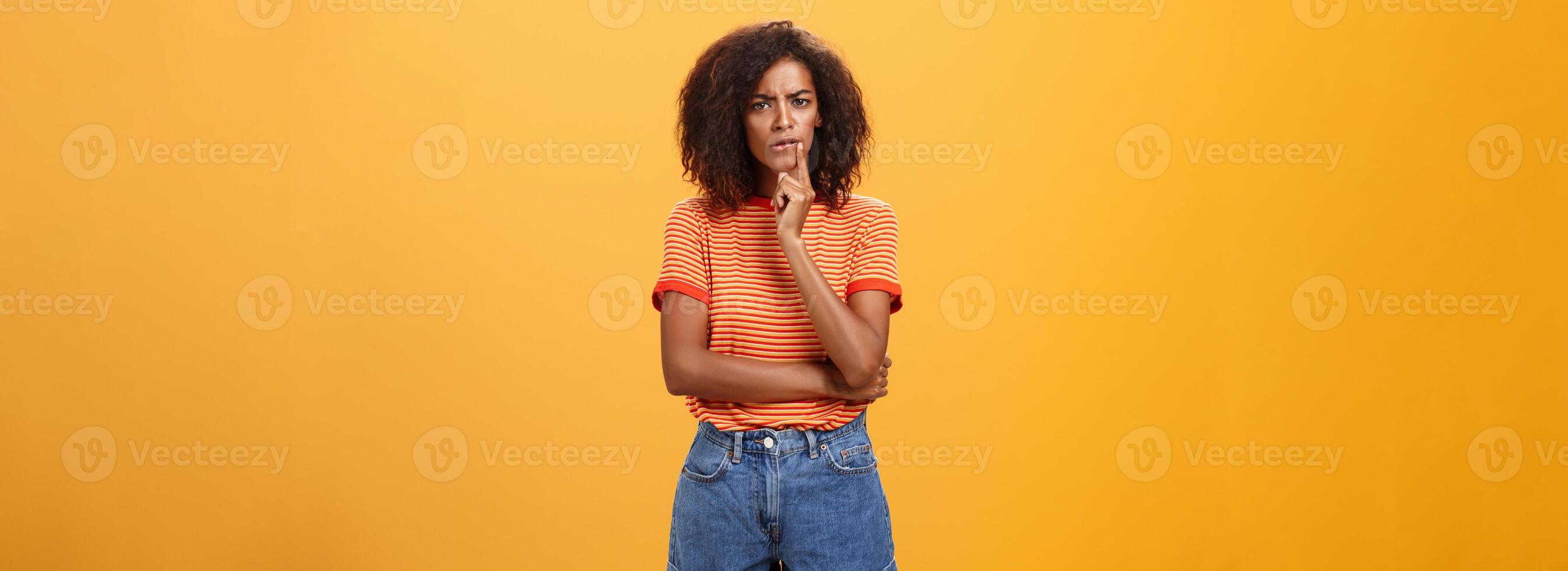 Woman looking concerned picking new furniture in store. Thoughtful focused and troubled smart african american businesswoman in casual outfit frowning biting lip touching mouth while thinking photo
