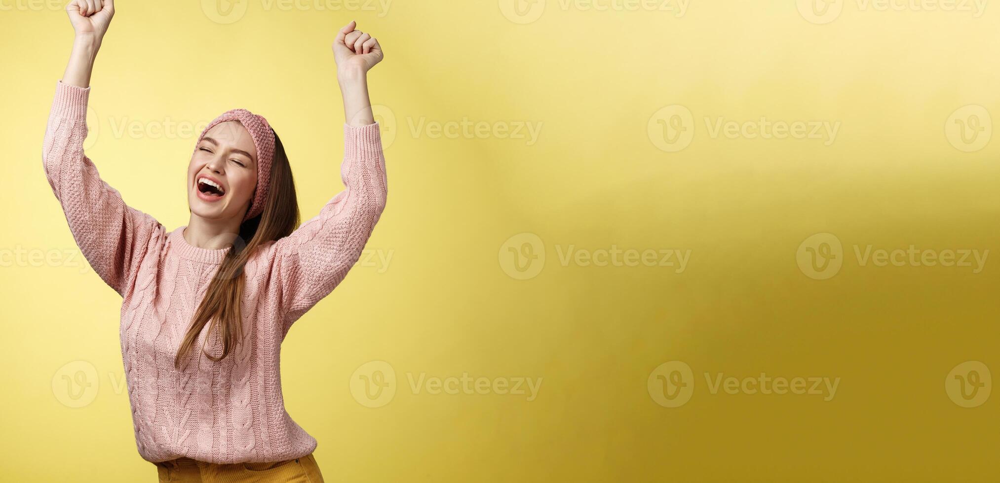 Positive celebating happy european young woman wearing casual sweater yelling happily shouting yes, triumphing racing hands up in success jumping ecstatic rejoicing cheerfully over success photo