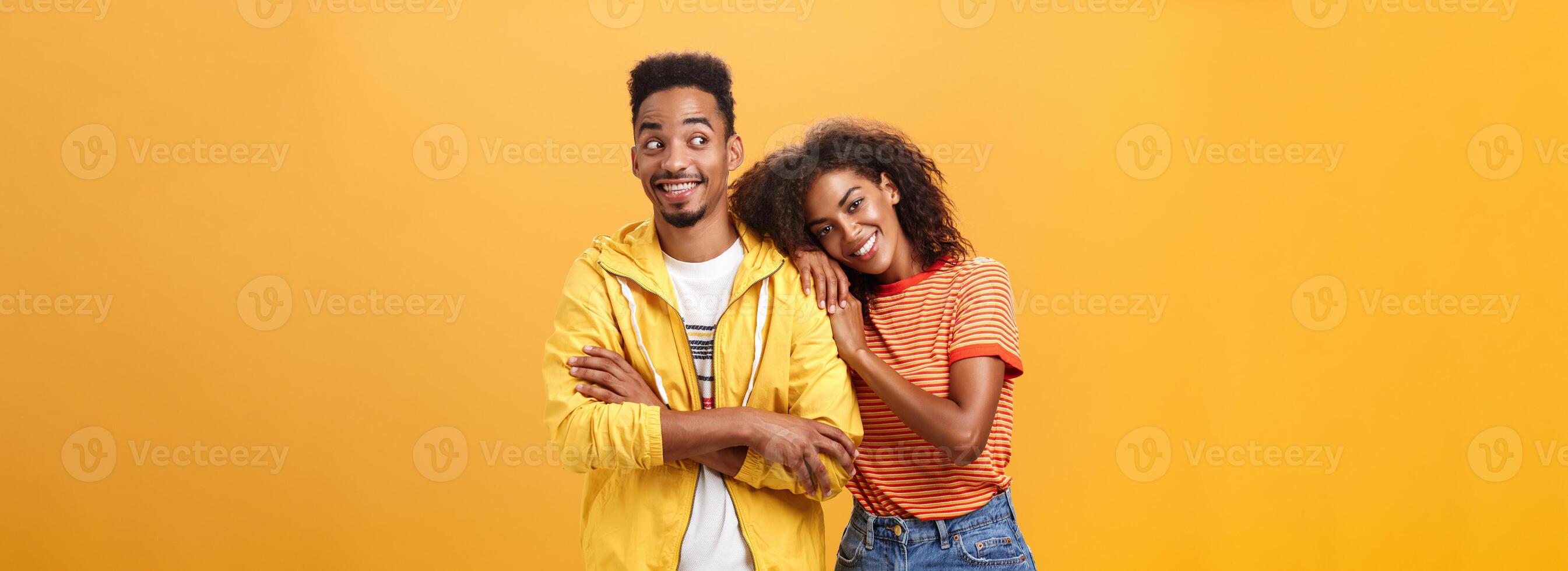 Guy feeling happy girl lean on his shoulder grinning and chuckling from happiness standing pleased and joyful over orange background while woman hugging best friend upbeat she can rely on him photo