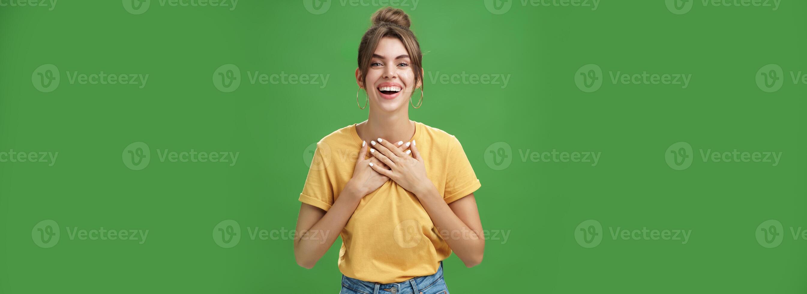 Encantado encantador mujer con brechado dientes en acogedor atuendo participación palmas en cofre en agradecido o agradecido actitud sonriente en general recepción calentar Felicidades en pie satisfecho, contento terminado verde pared foto