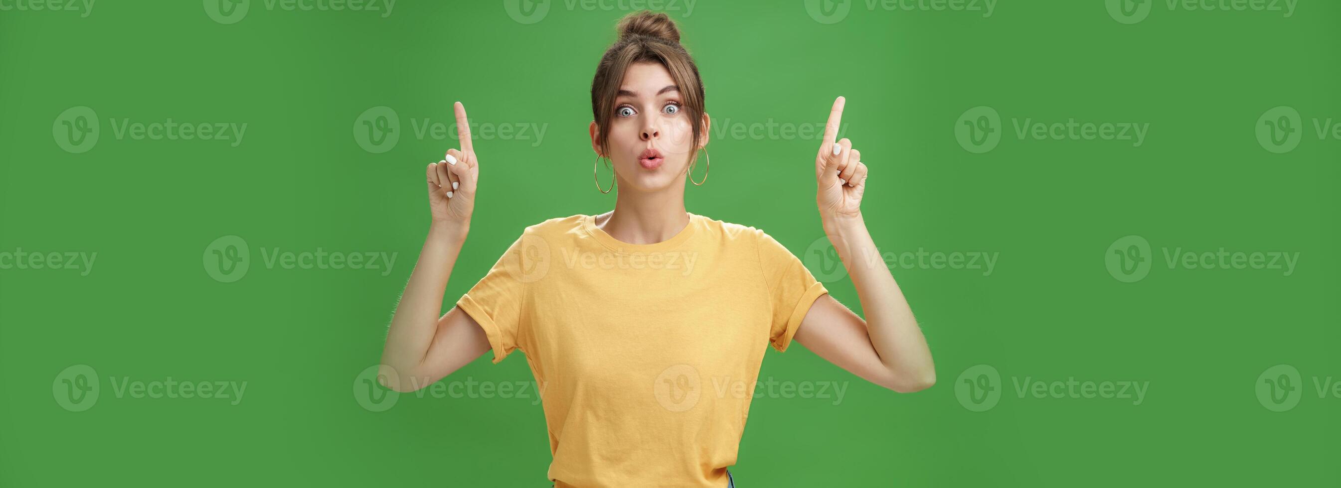 Authentic good-looking woman with natural beauty and tattoo on arm raising index fingers pointing up folding lips from interest and curiosity reacting impressed and excited at awesome advertisement photo