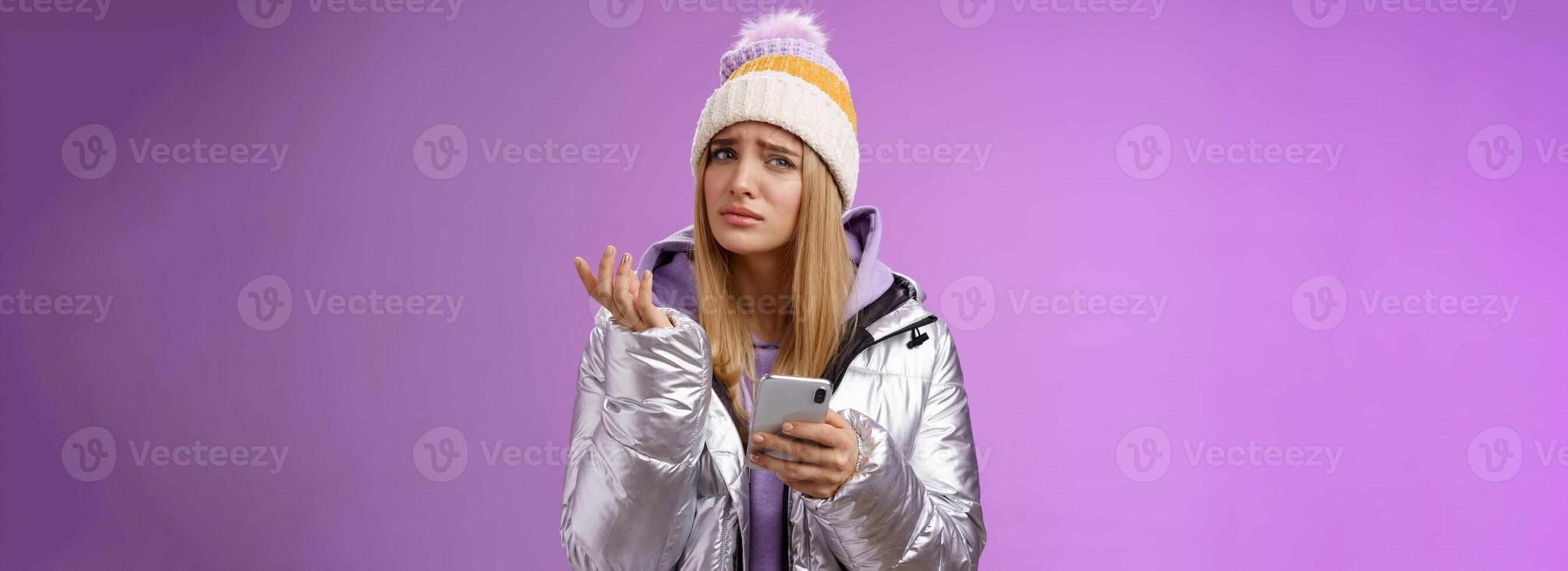 Questioned complicated cute blond girlfriend receive strange message look perplexed confused raising hand shrugging lift eyebrow cannot understand meaning holding smartphone, purple background photo