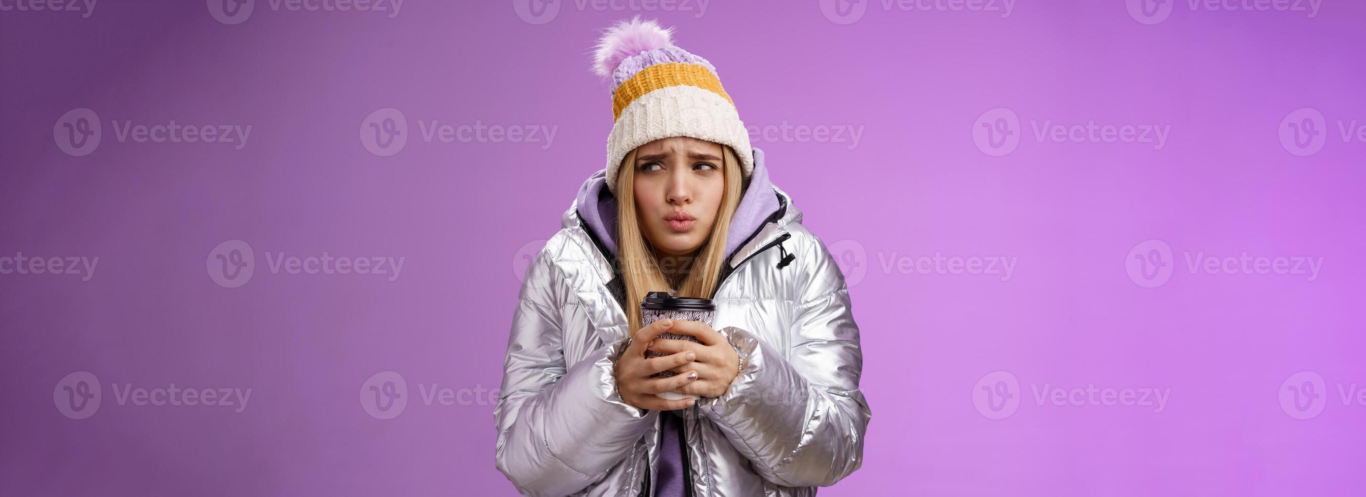 Trembling uncomfortable cute pouting young blond girl feel freezing cold winter snowy weather outside shaking low temperature hold take-away hot coffee cup warming up, purple background photo