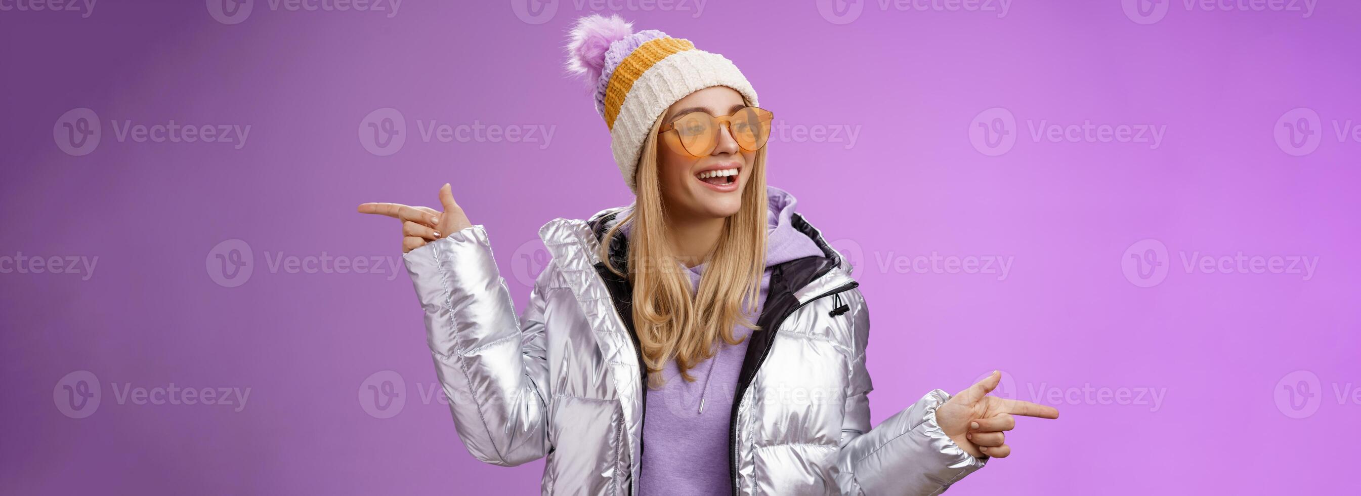 Cool sassy friendly-looking blond girl pointing different sides right left choose which way go look delighted carefree enjoy awesome winter vacation wear stylish silver jacket, hat sunglasses photo