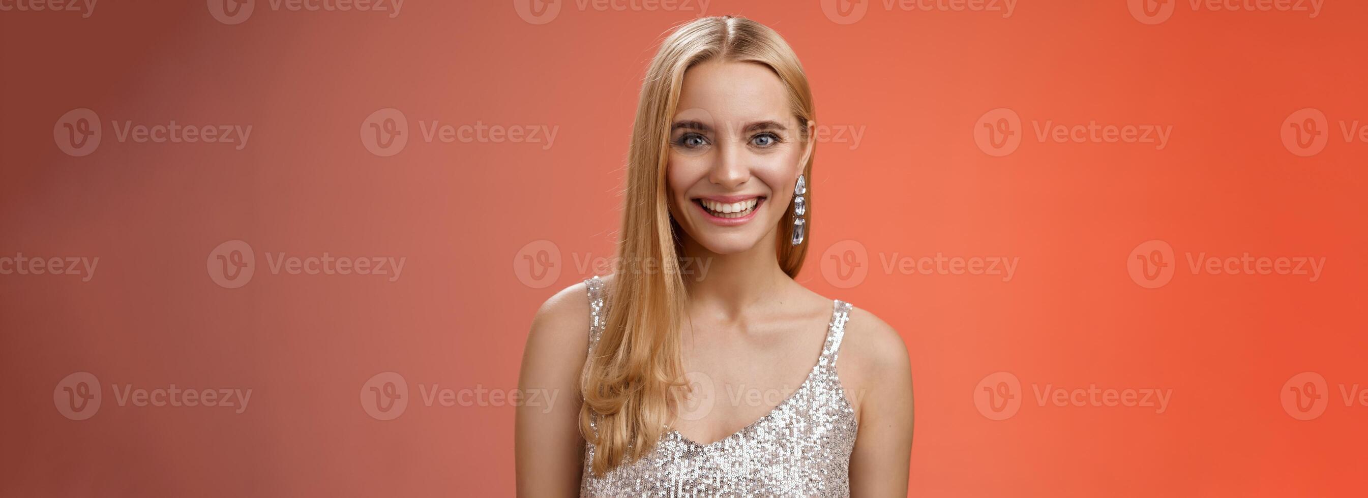 Charming glamour fabulous adult 25s blond woman in elegant silver dress shiny earrings smiling happily take part interesting conversation talking look friendly grinning, standing red background photo
