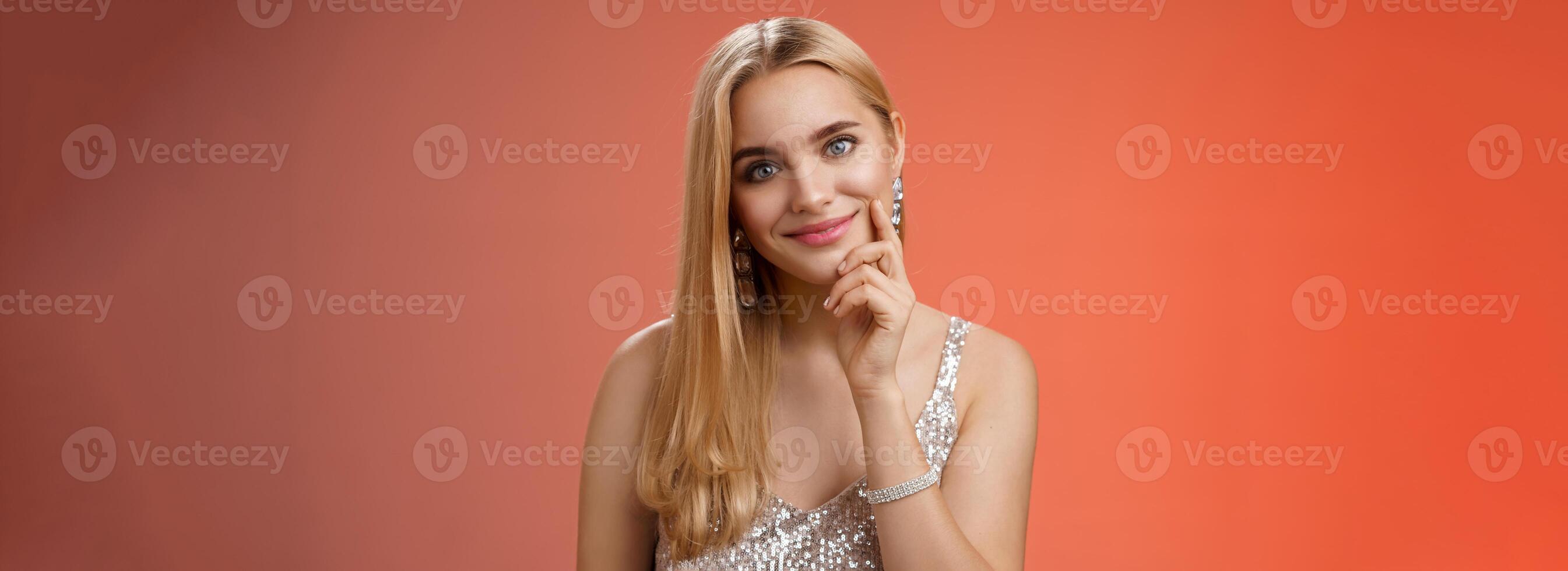 Tender feminine glamour young lady in silver glittering dress accessorize touching cheek flirty look camera smiling delighted use seduction skills ask man buy drink nightclub photo