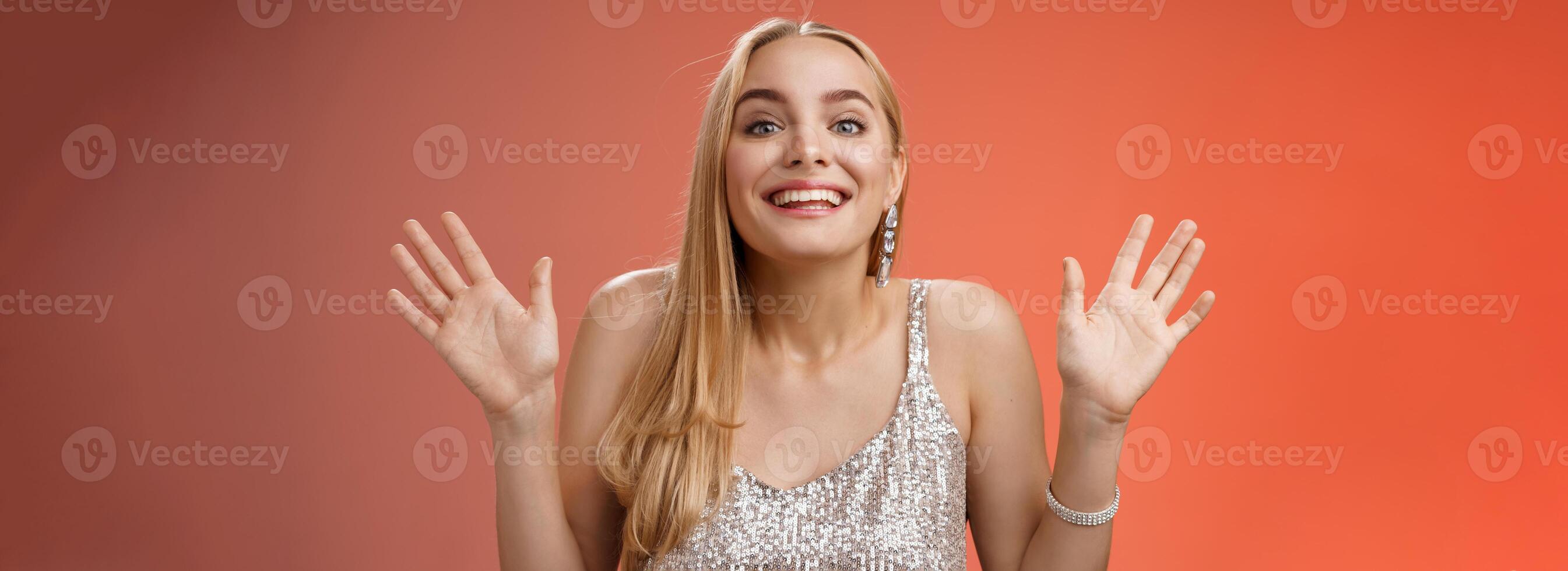 Happy elegant dreamy glamour young blond woman raising hands delight joyfully smiling camera glad see friends comming party welcoming guests grinning happily, wearing silver stylish dress photo