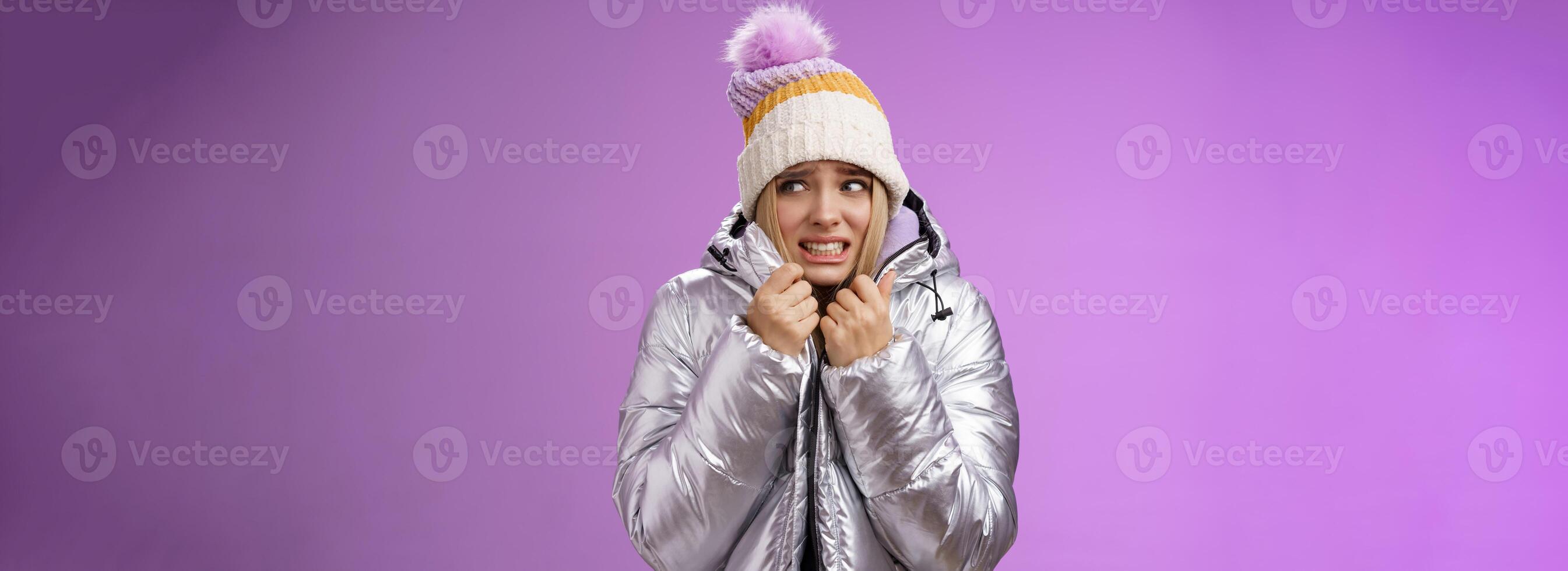 Freezing uncomfortable trembling cute blond girl in hat pull jacket tight feeling cold walking snowy mountains low temperature clenching teeth stooping shaking, standing upset purple background photo