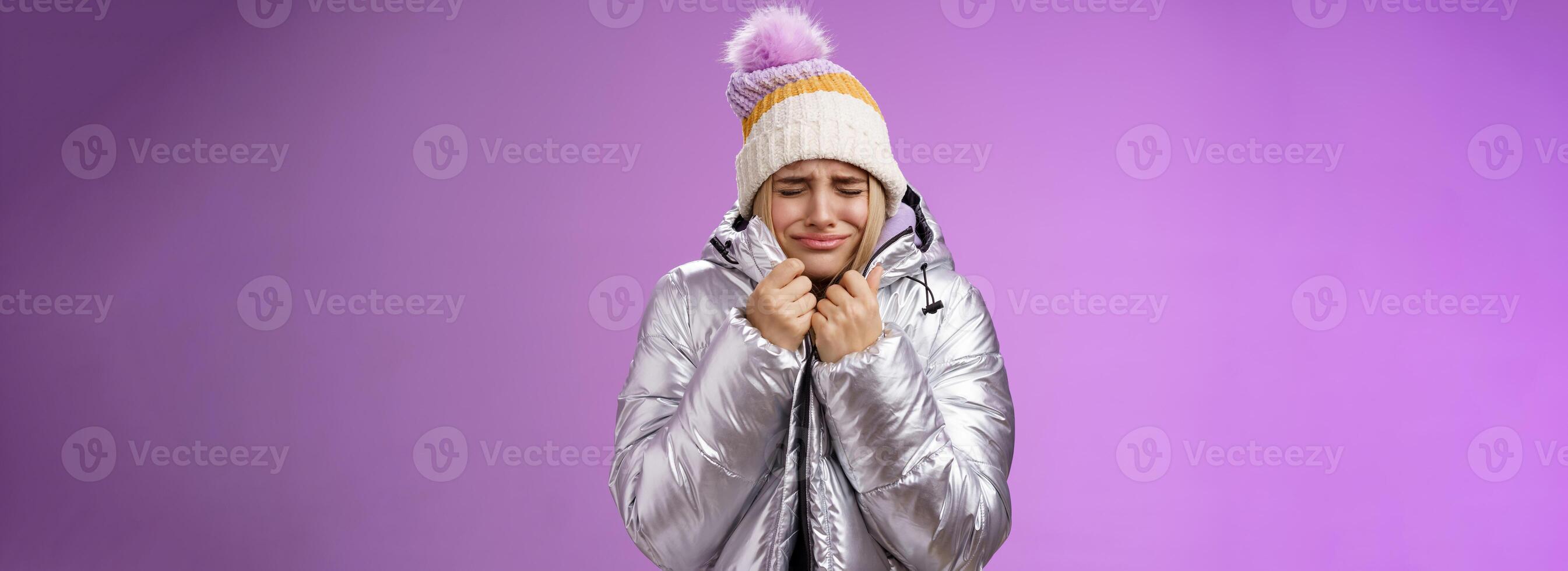 Unhappy sobbing whining cute blond girl pull jacket tight body close eyes crying freezing cold standing snowy winter resort shaking low temparature, purple background suffering discomfort photo