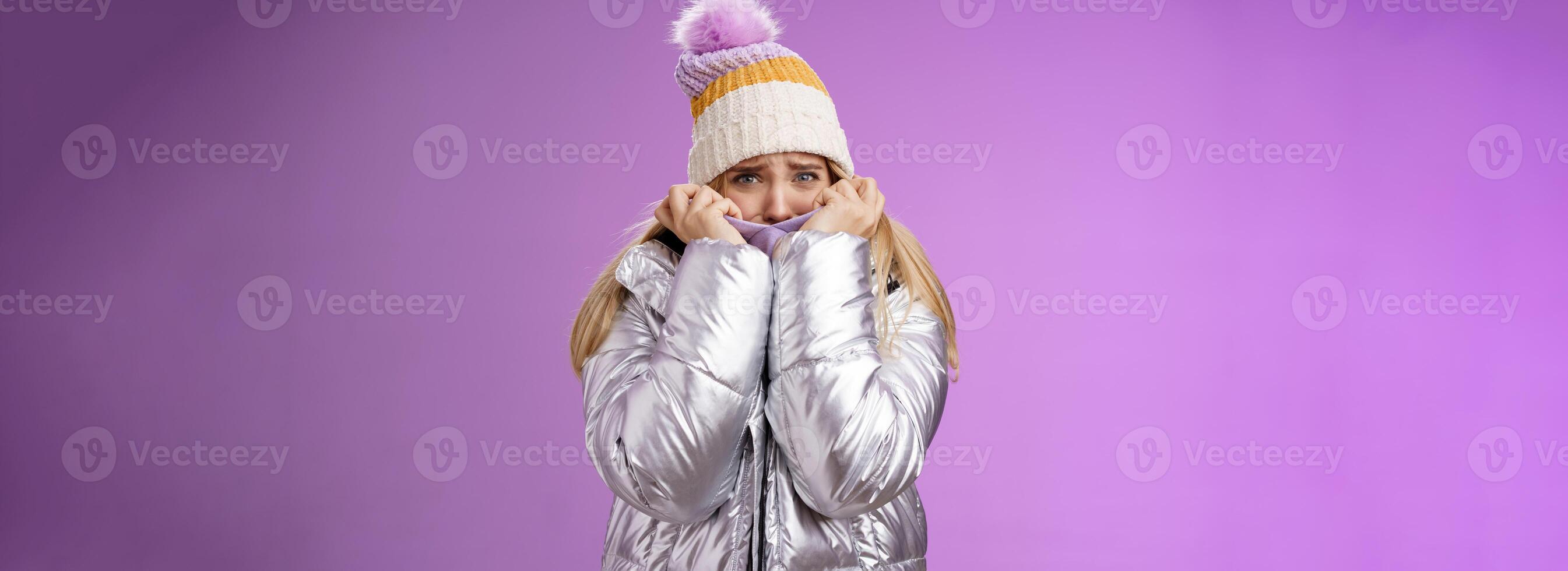 Scared afraid insecure coward girl in cute hat glittering shiny jacket pull cloth face frightened frowning stooping look concerned terrified scared death, standing purple background timid photo