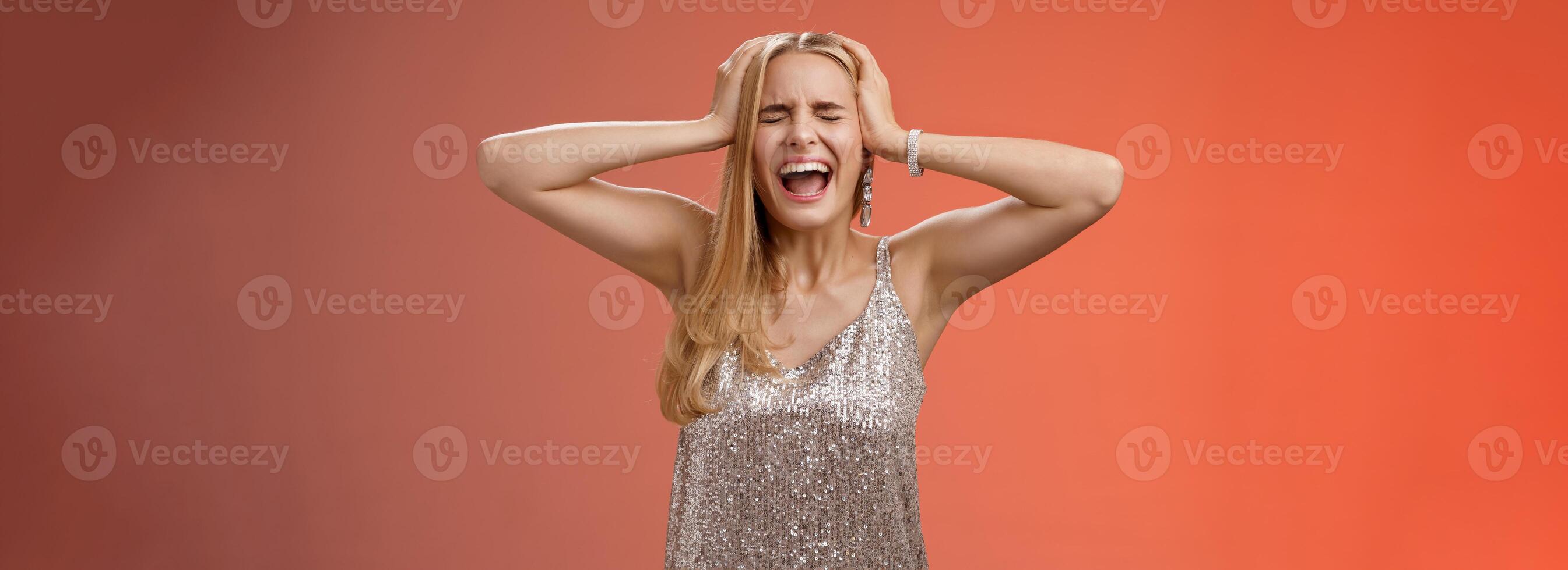 Upset distressed pressured fed up panicking young blond woman in dress scream cry heart out being heartbroken close eyes hold hands head mentaly unstable standing sad depressed red background photo