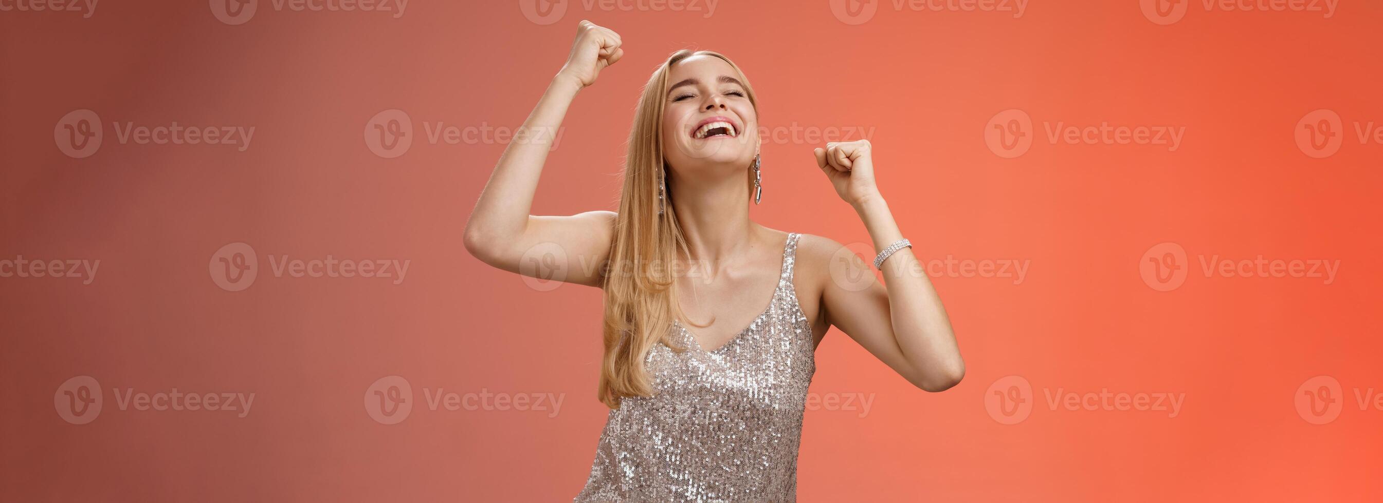 Excited carefree happy stylish blond european woman having fun dancing smiling broadly laughing happiness enjoying awesome music party rocking lighting dance-floor standing red background photo