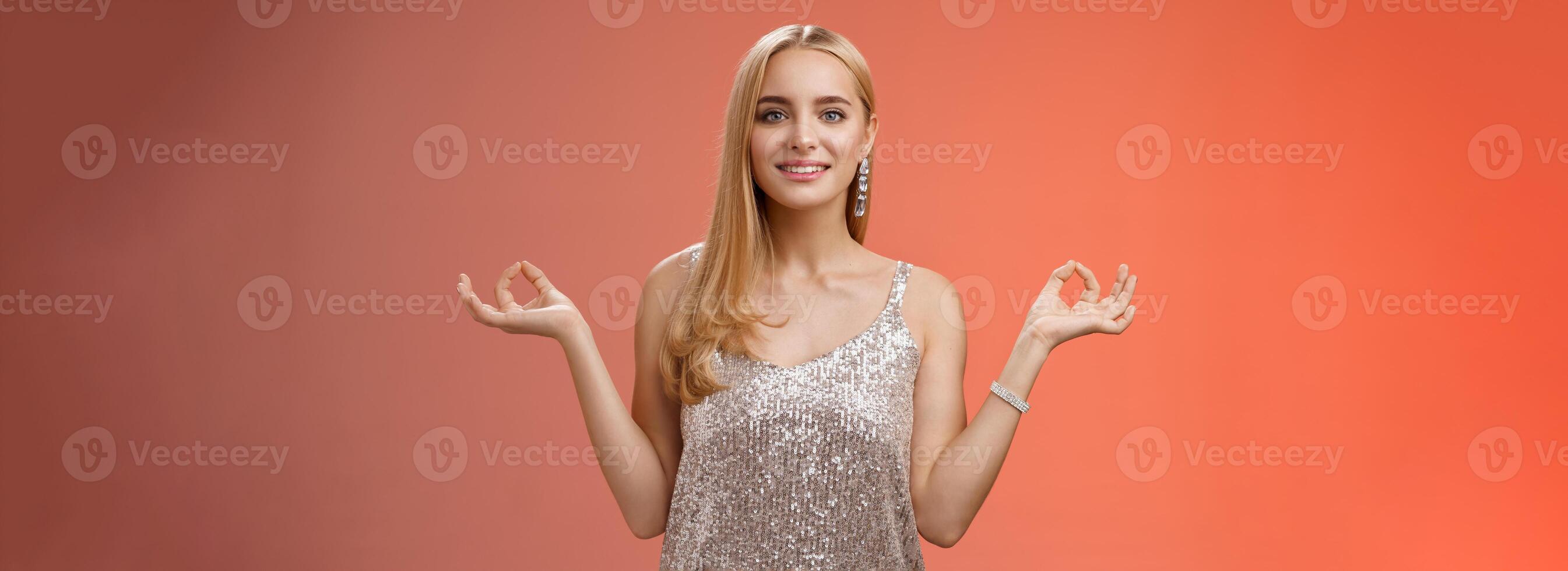 Calm relieved happy fabulous young blond woman in silver stylish luxury dress standing relaxed red background zen lotus pose reach nirvana smiling peaceful carefree meditating breathing practice photo