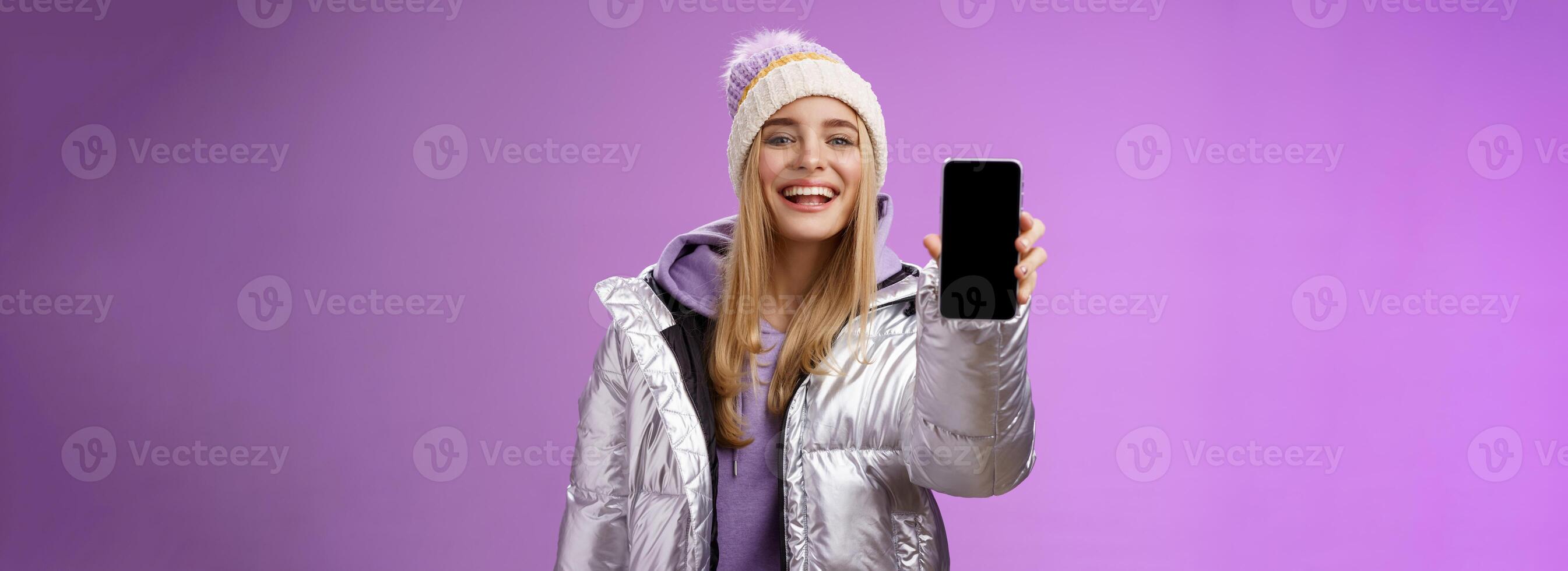 Sassy delighted cheerful blond woman recommend use app edit perfect pictures holding smartphone showing mobile phone display proudly satisfactory smile camera, standing purple background photo