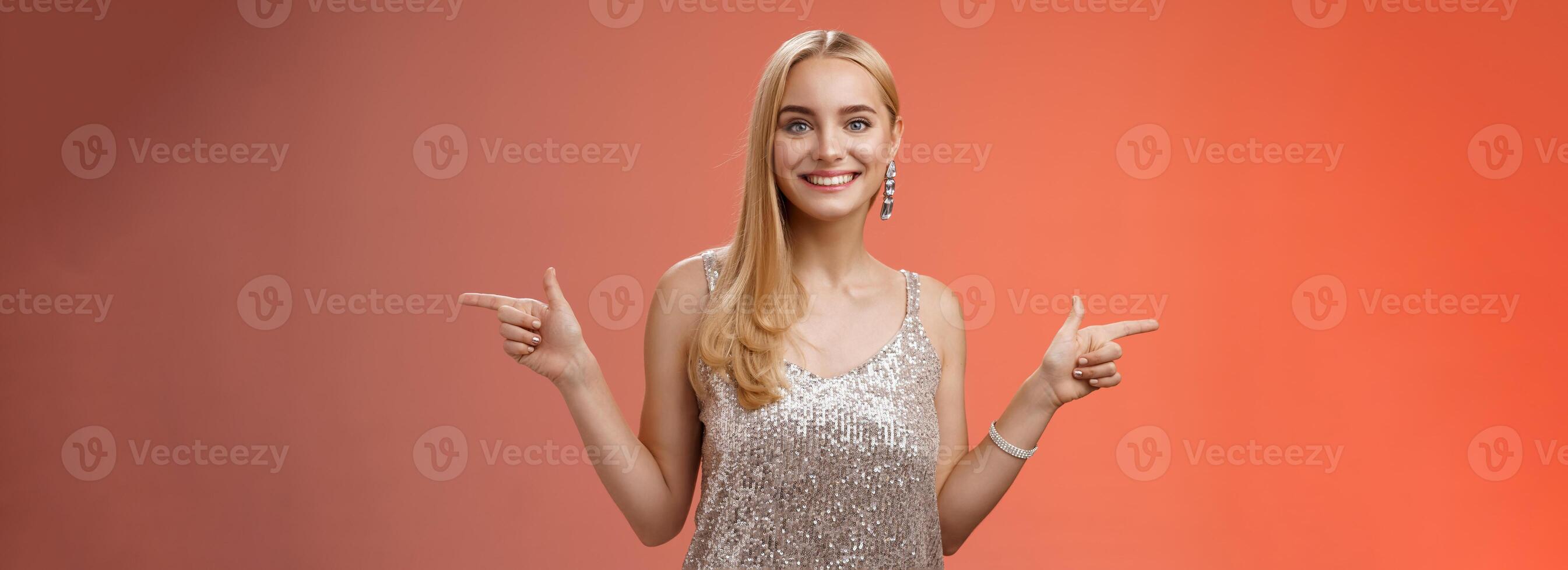 Waist-up shot energized cheerful blond european girl in silver glittering dress pointing sideways left right smiling amused showing lots variants variety opportunities make choice which better photo