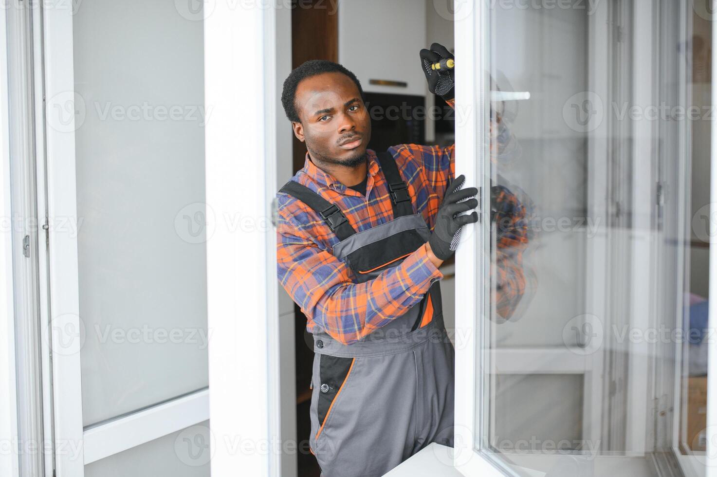 Workman in overalls installing or adjusting plastic windows in the living room at home photo