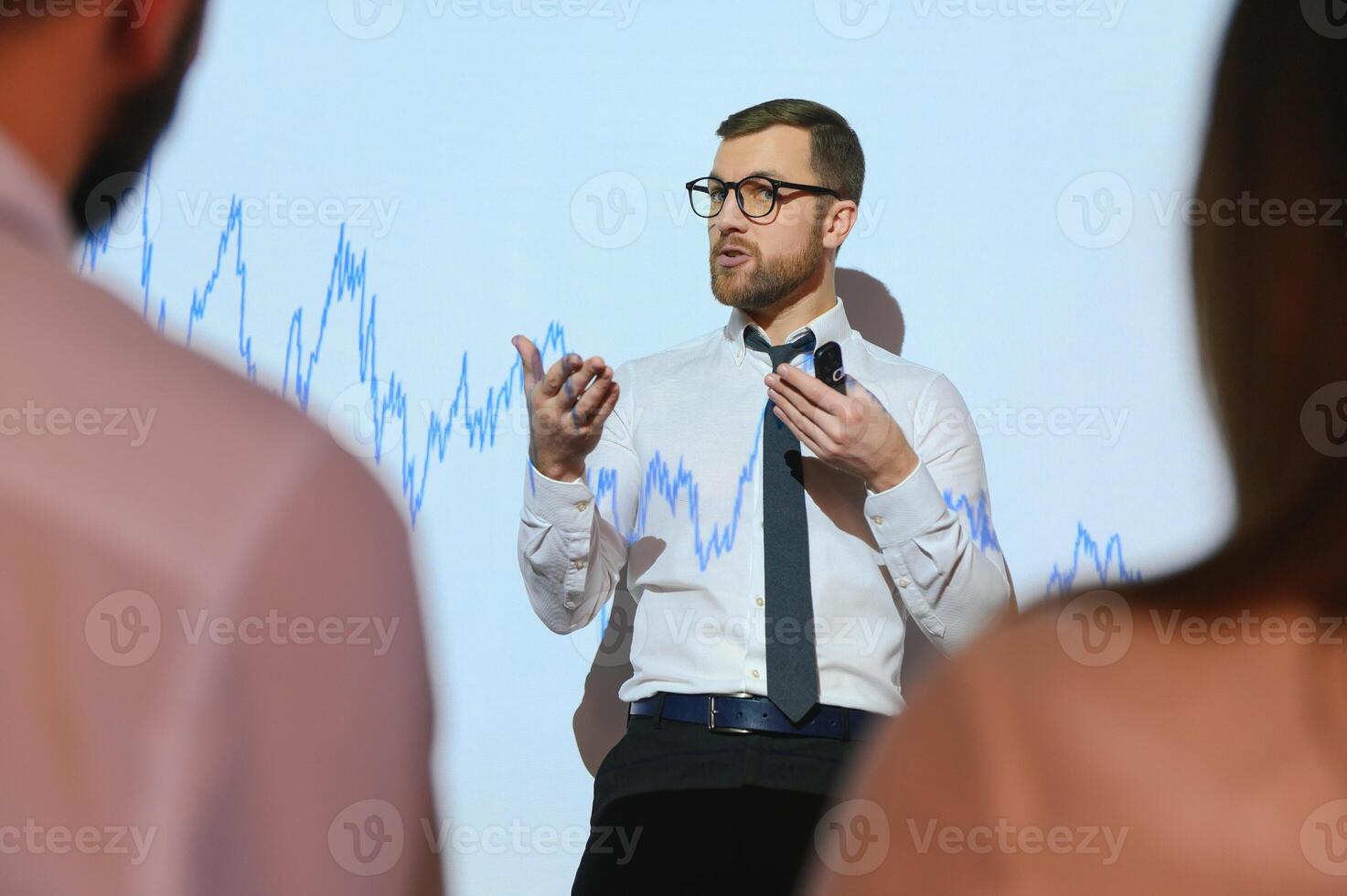 Man is standing near projector and showing graphs and business graphs. photo