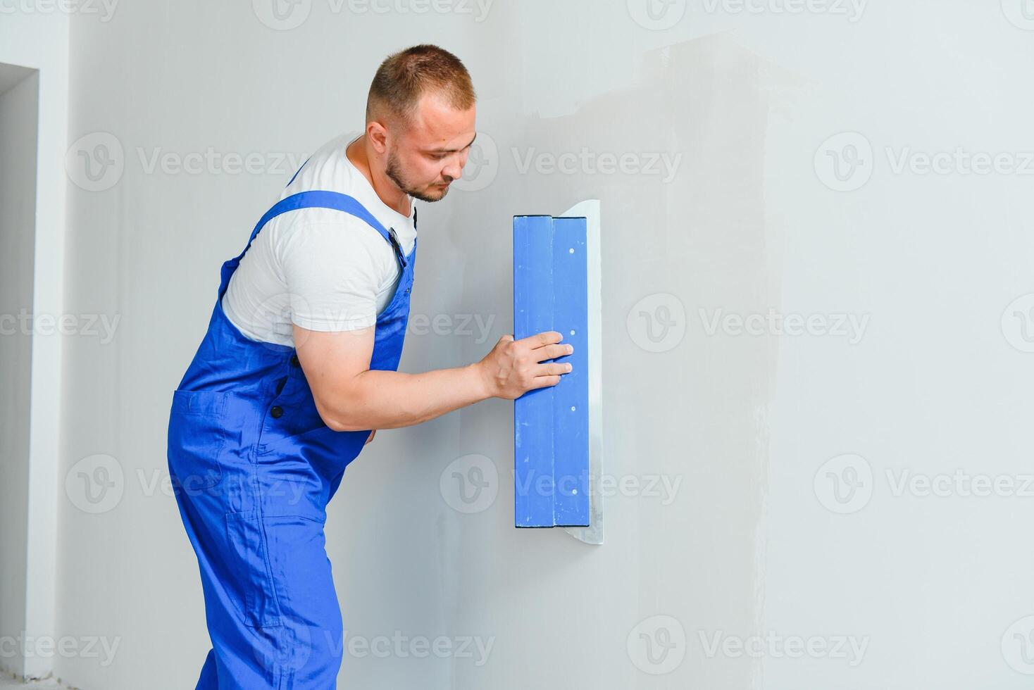 A general laborer in overalls uses a trowel to cover the wall with cement photo
