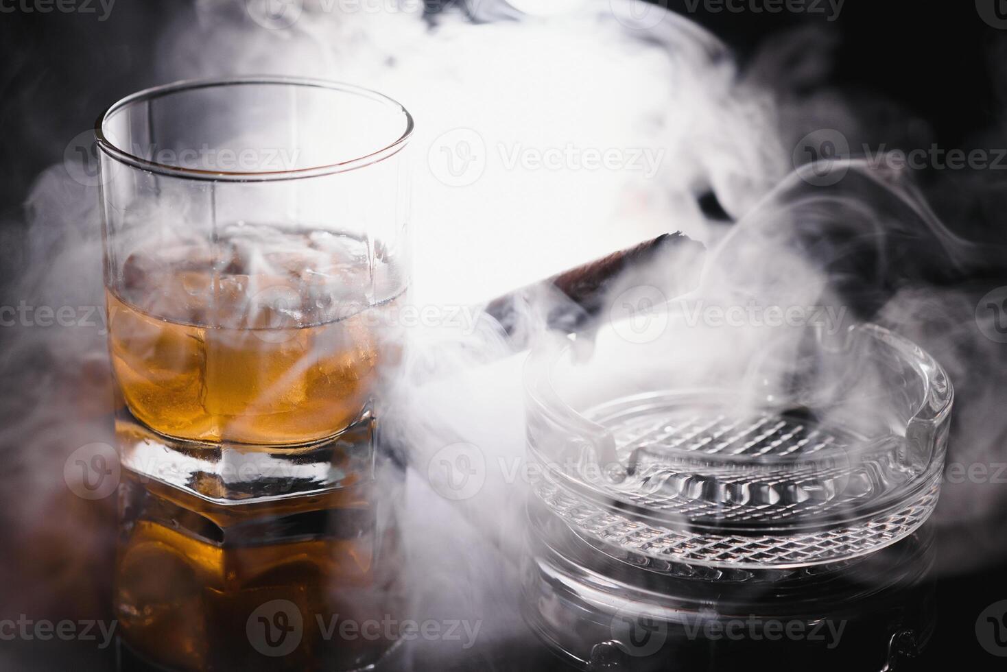 Glass of cold whiskey with cigar on dark background photo