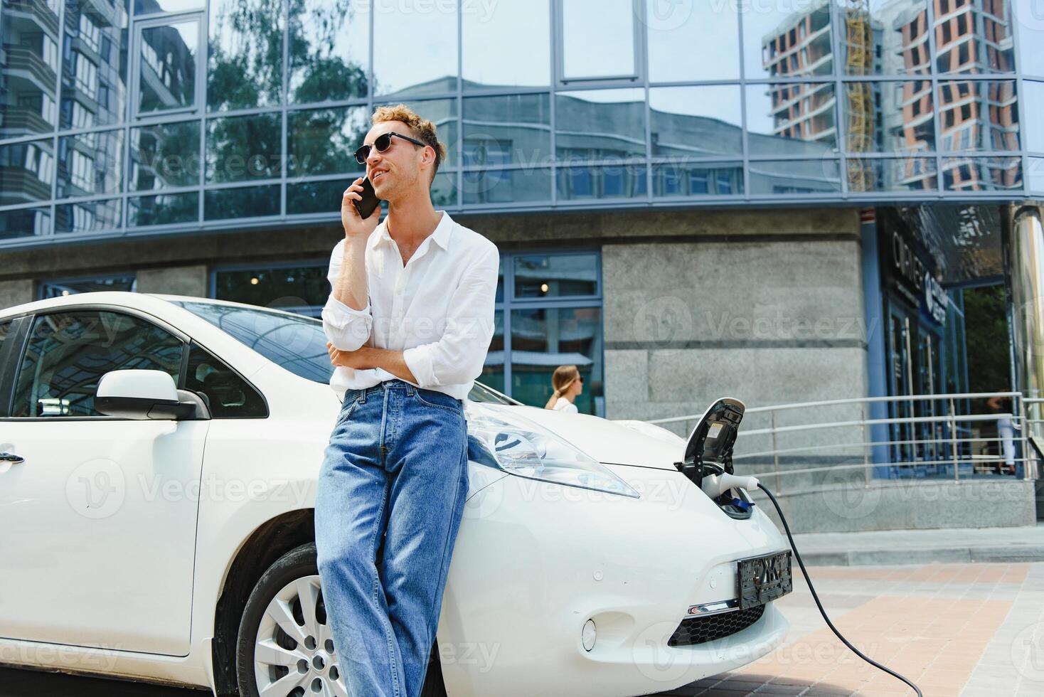 Handsome man using phone while car being charged photo