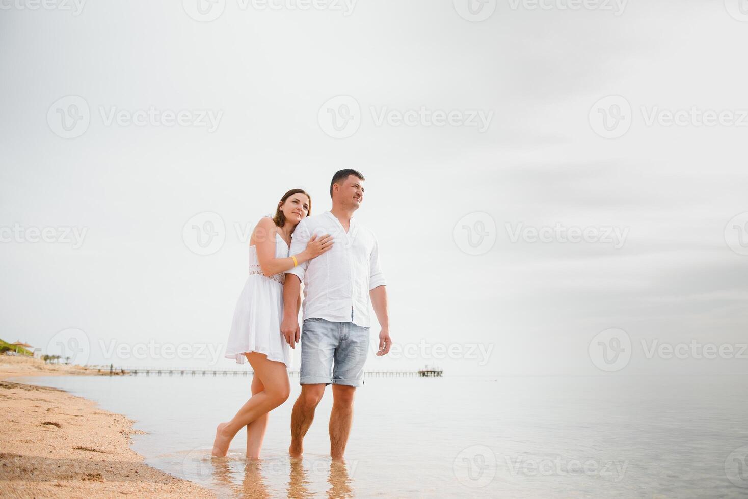 Vacation couple walking on beach together in love holding around each other. Happy interracial young couple, Asian woman and Caucasian man. photo