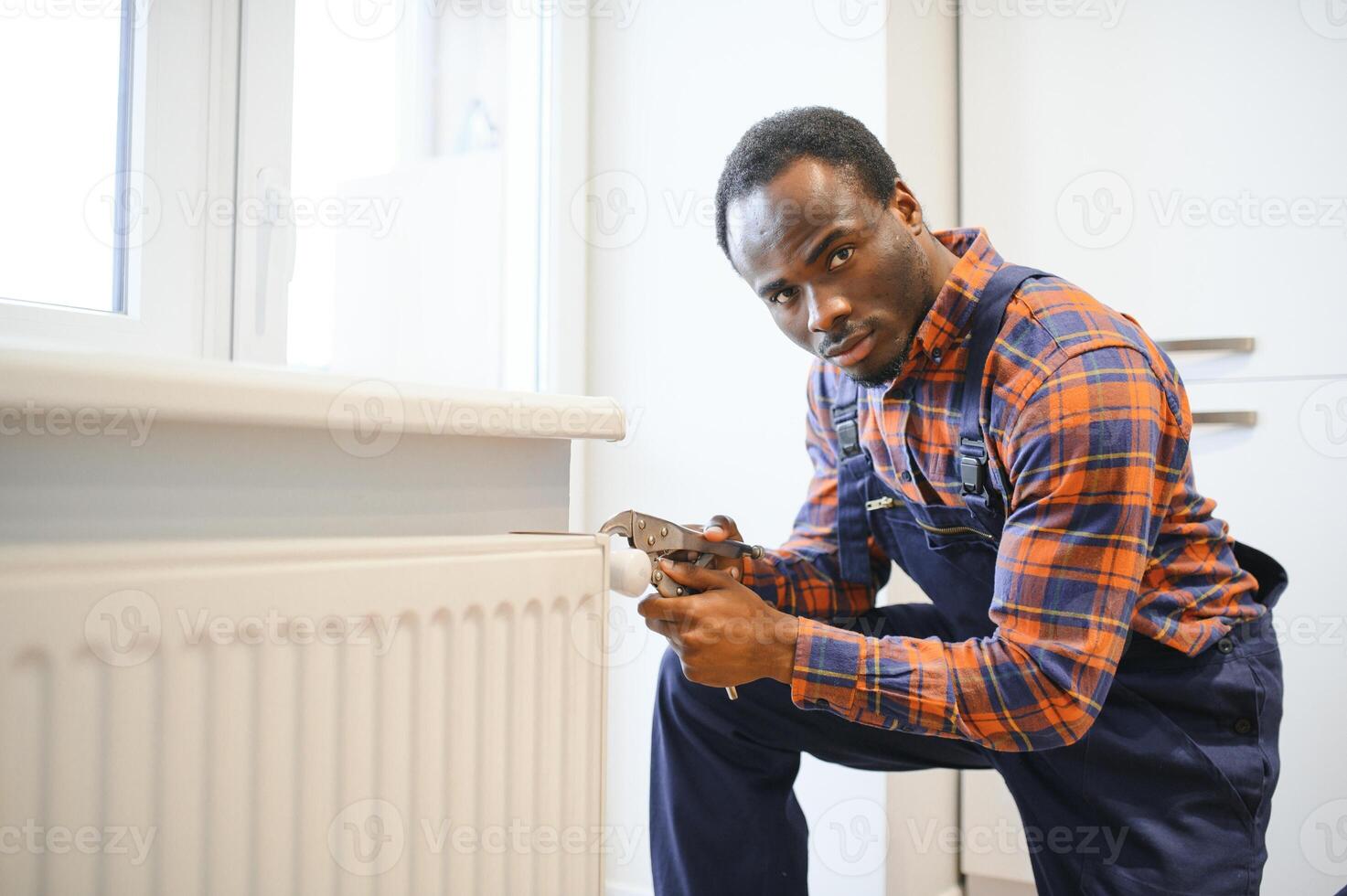 Repair heating radiator close-up. African man repairing radiator with wrench. Removing air from the radiator photo