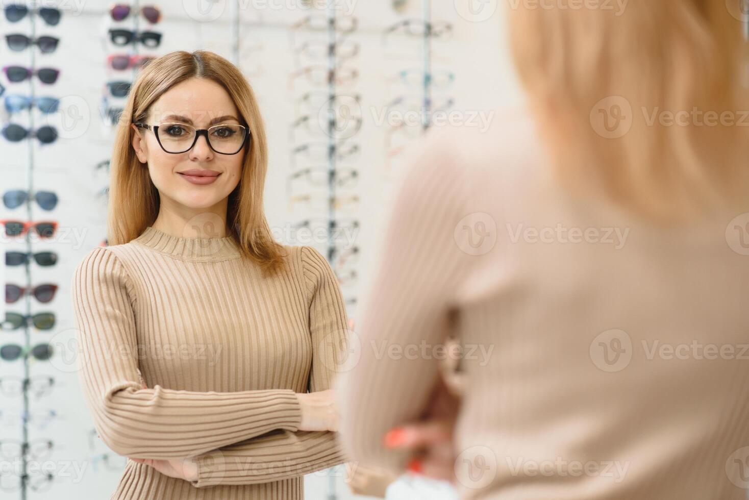 Pretty young woman is choosing new glasses at optics store. photo