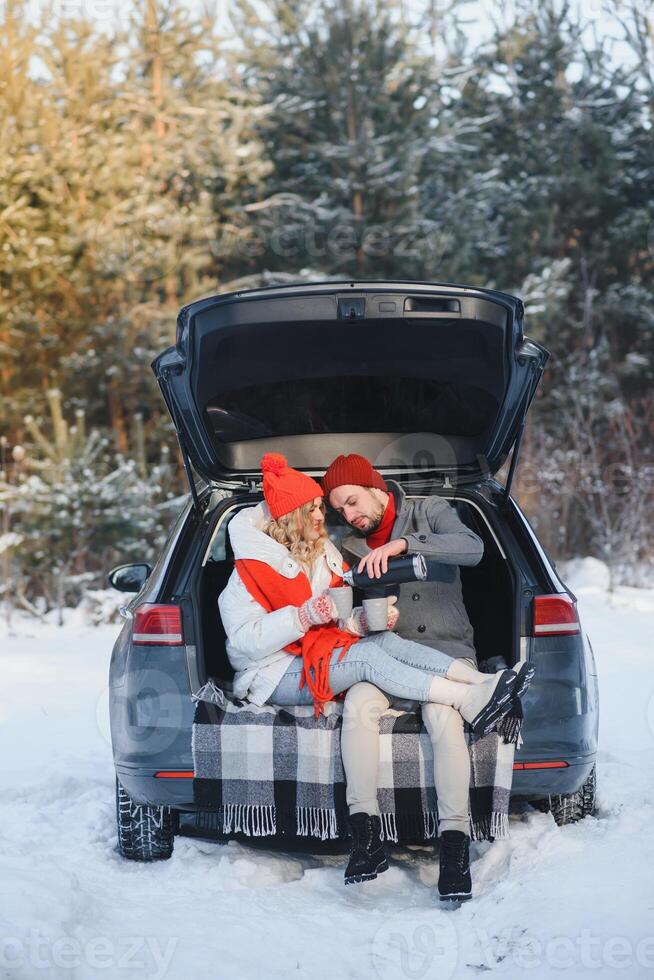 Cute Couple Having Winter Forest Picnic Drinking Tea from Tea Take Away Cup. Nature Picnic. Love Story Date at Car. photo