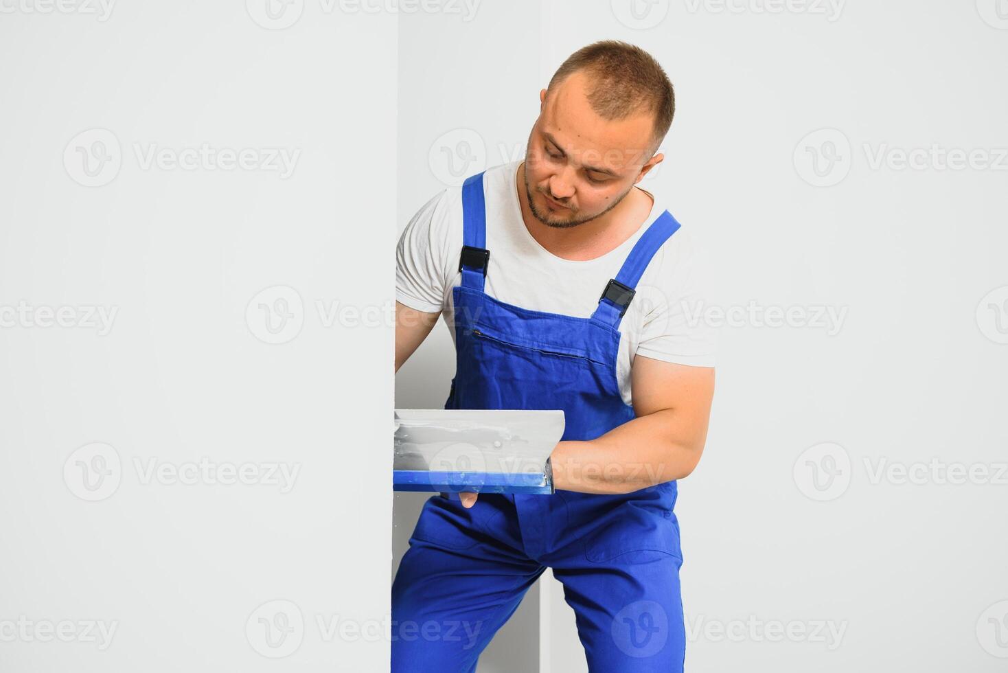 The builder carefully corrects the irregularities of the wall with a trowel. Builder in work clothes against a gray wall. Photo plasterer at work.