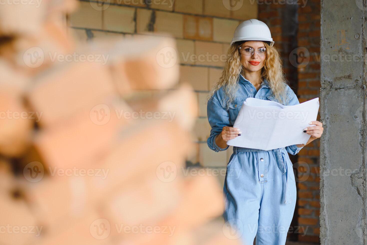 Construction concept. Pretty female builder in overalls and helmet working on construction site. photo