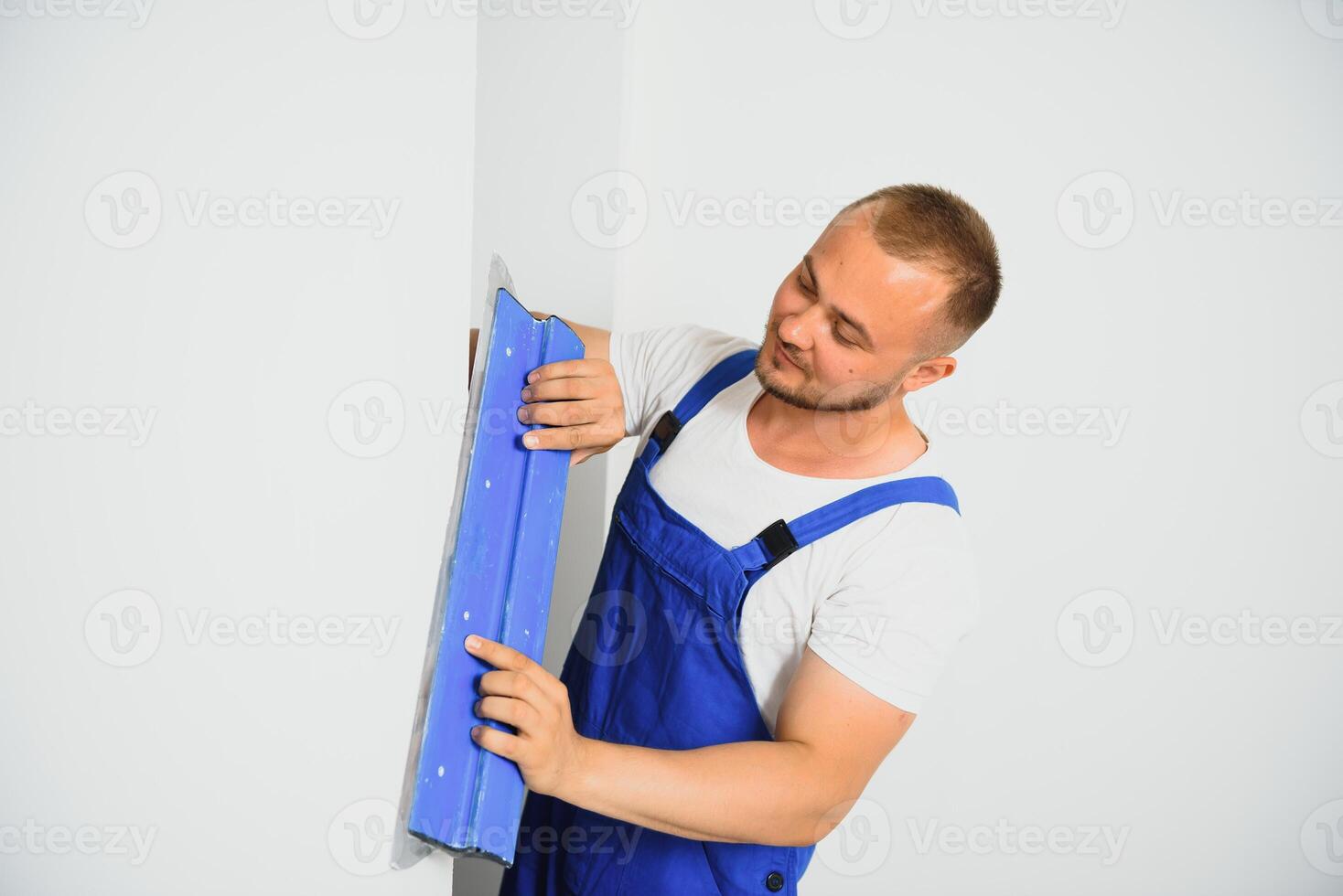 A man in overalls uses a trowel to cover the wall with cement photo