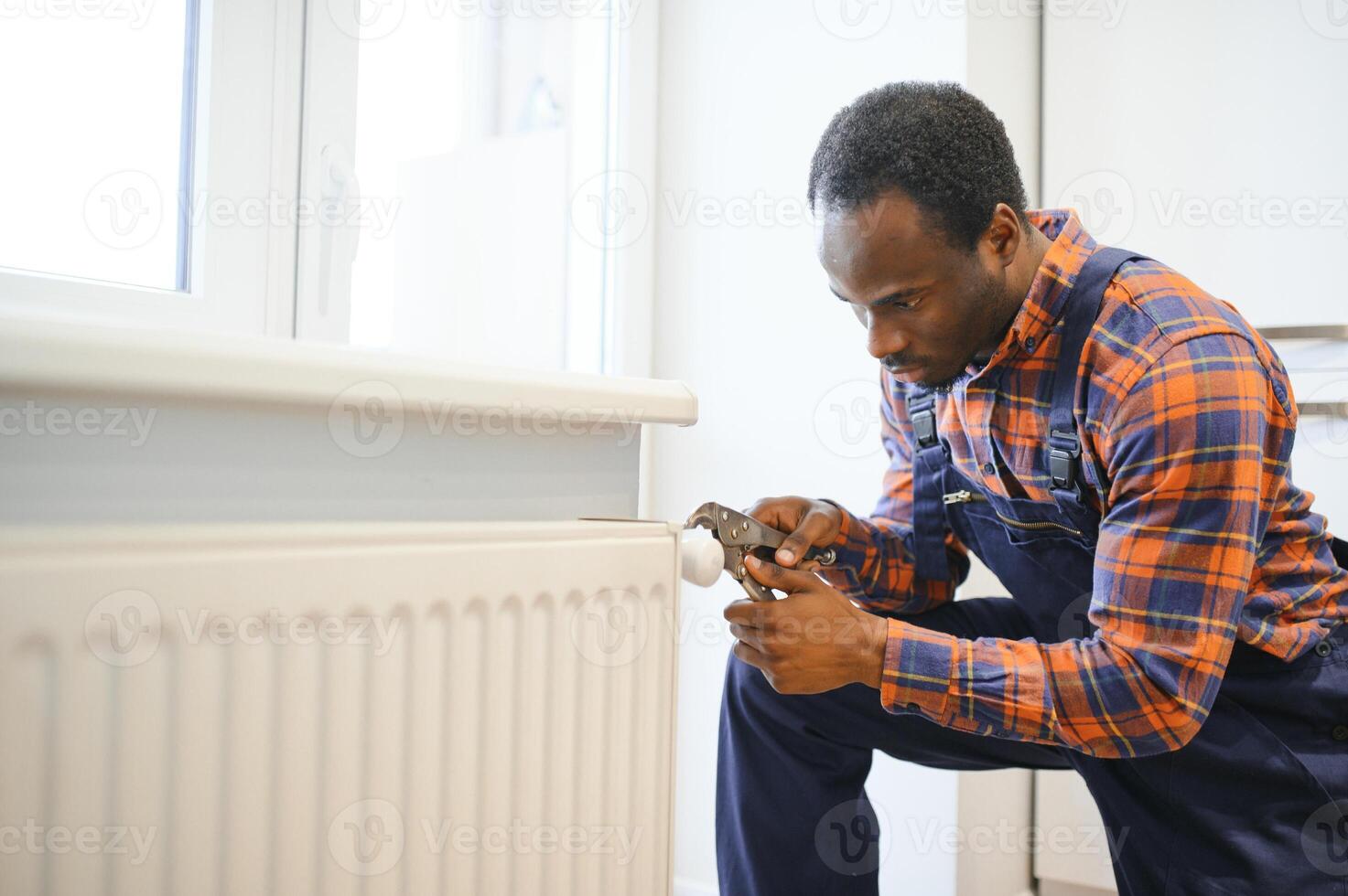 hombre en ropa de trabajo mono utilizando herramientas mientras instalando o reparando calefacción radiador en habitación foto