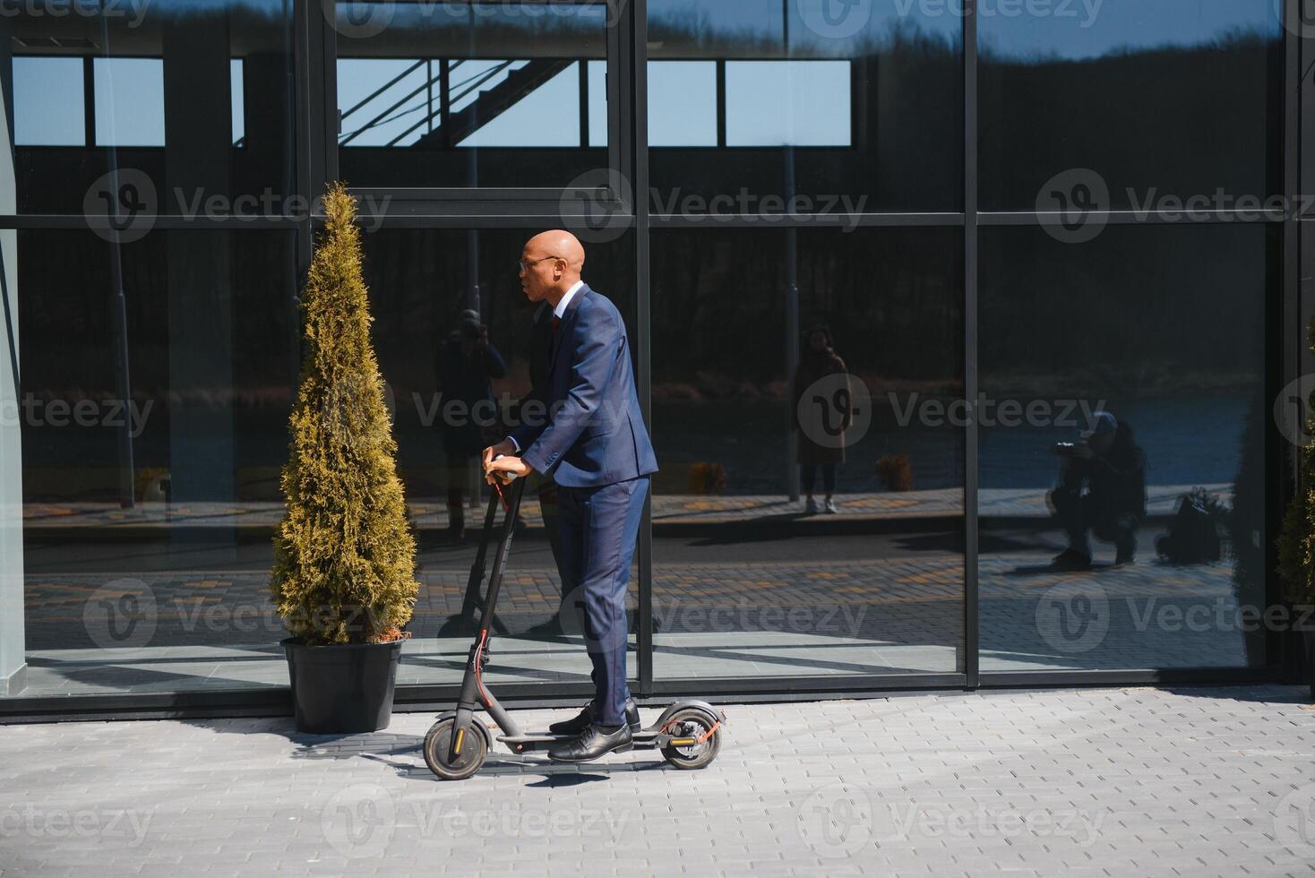 Handsome african 30s man wearing coat smiling while riding electric scooter outdoors photo