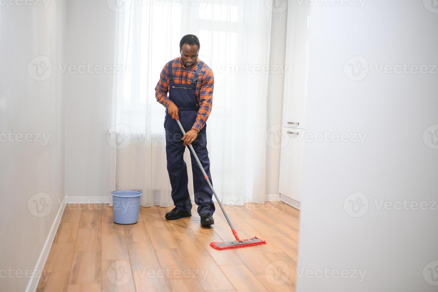 joven africano hombre lavados el piso con un fregona en el habitación foto